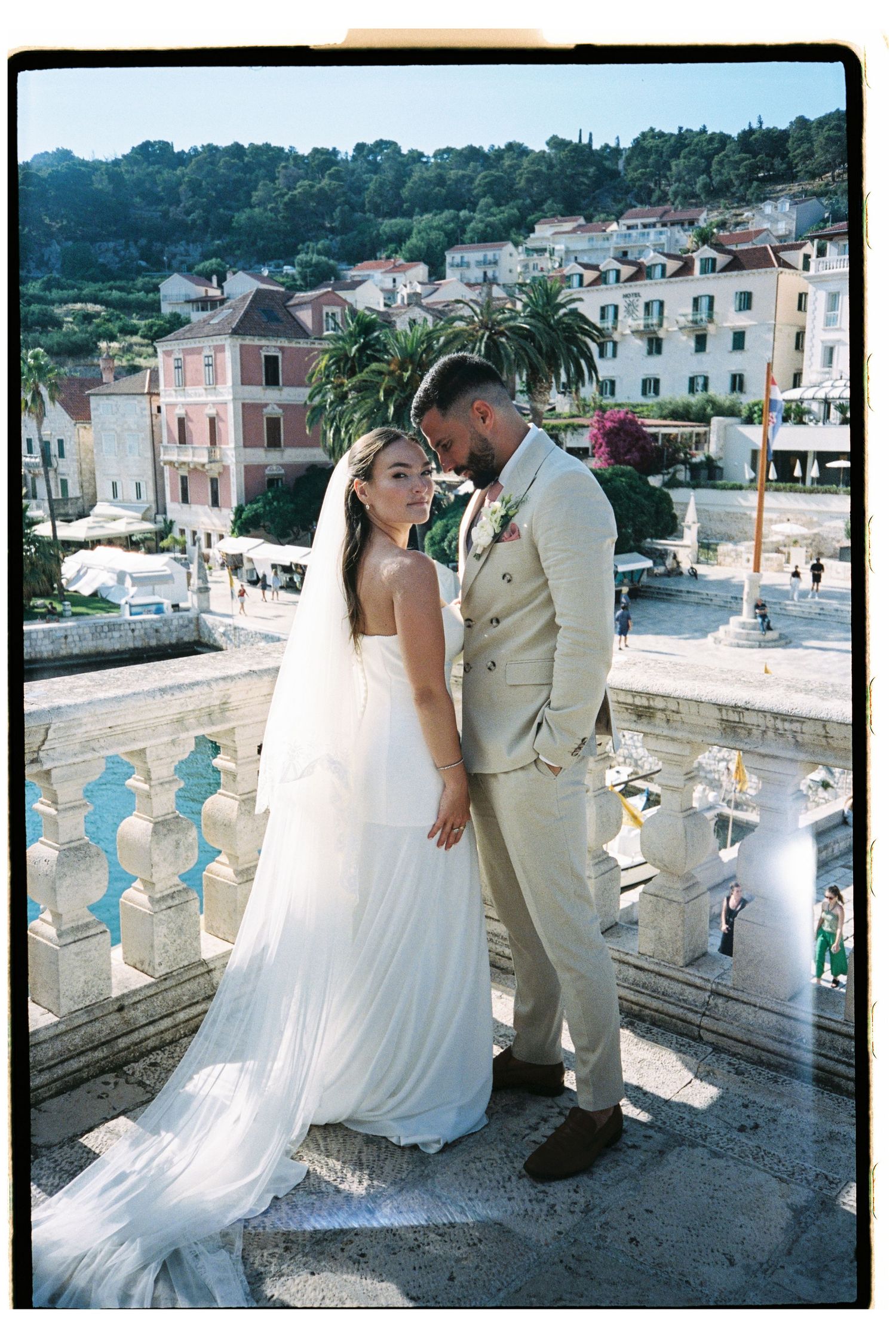Bride and groom share romantic moment on balcony overlooking coastal village.
