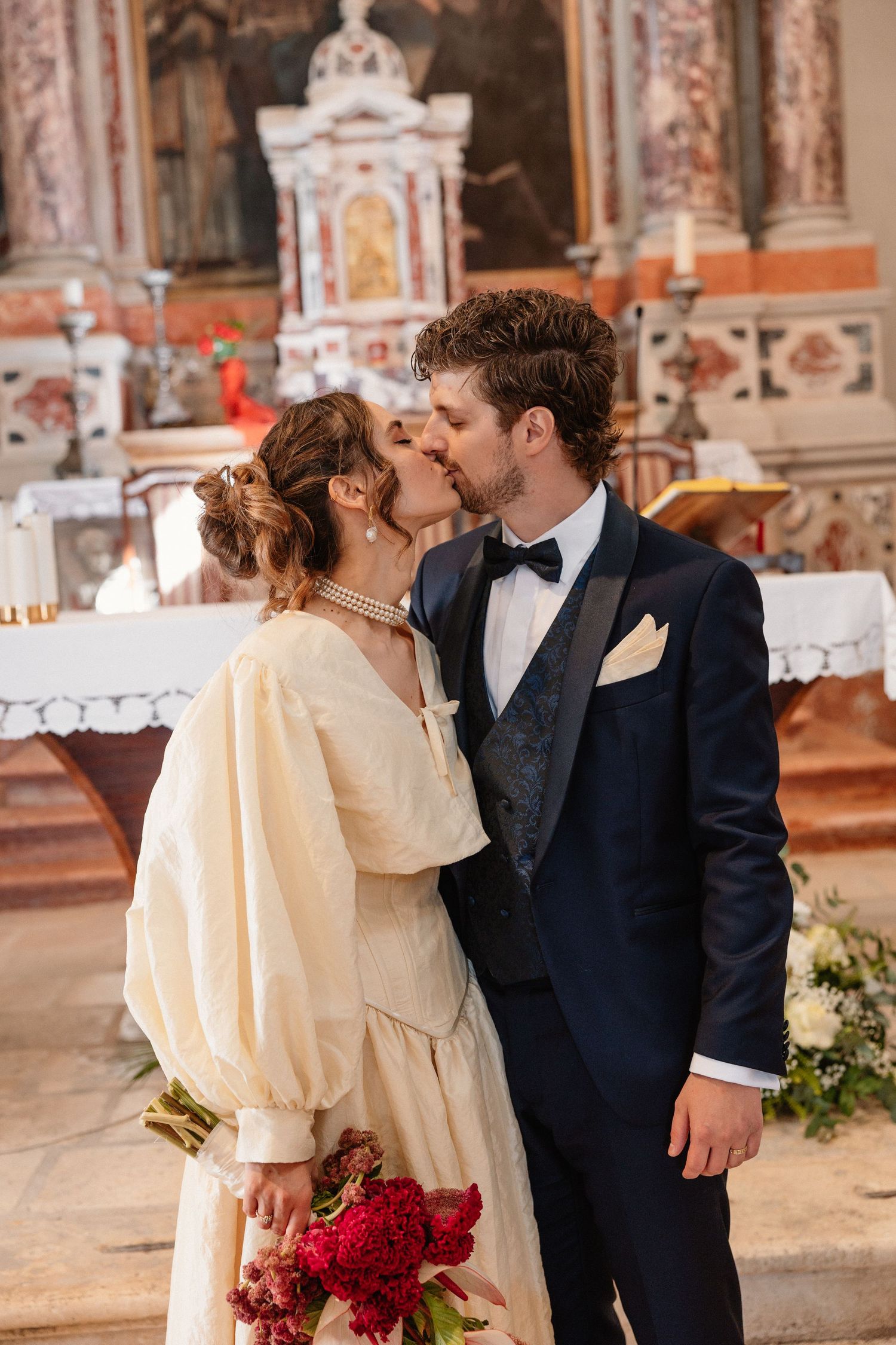 Romantic wedding kiss sequence inside an ornate church with red floral decorations.
