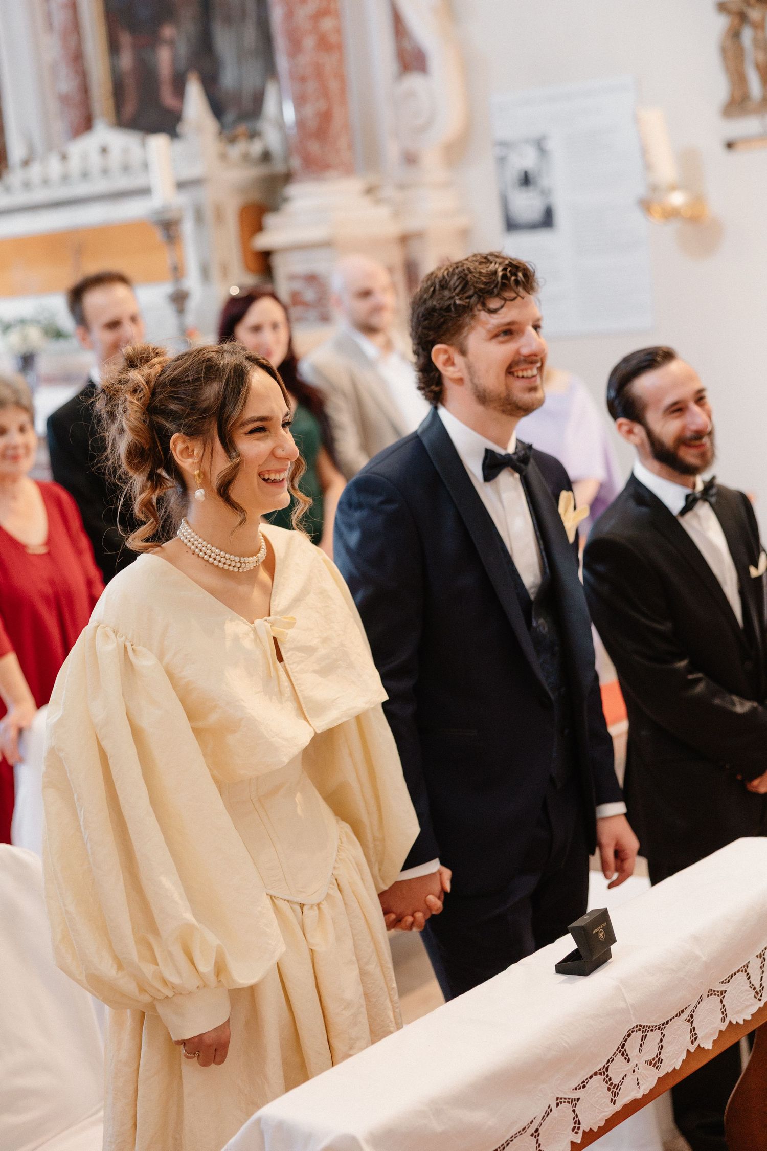Wedding guests in formal attire gathered in a church with ornate decor.