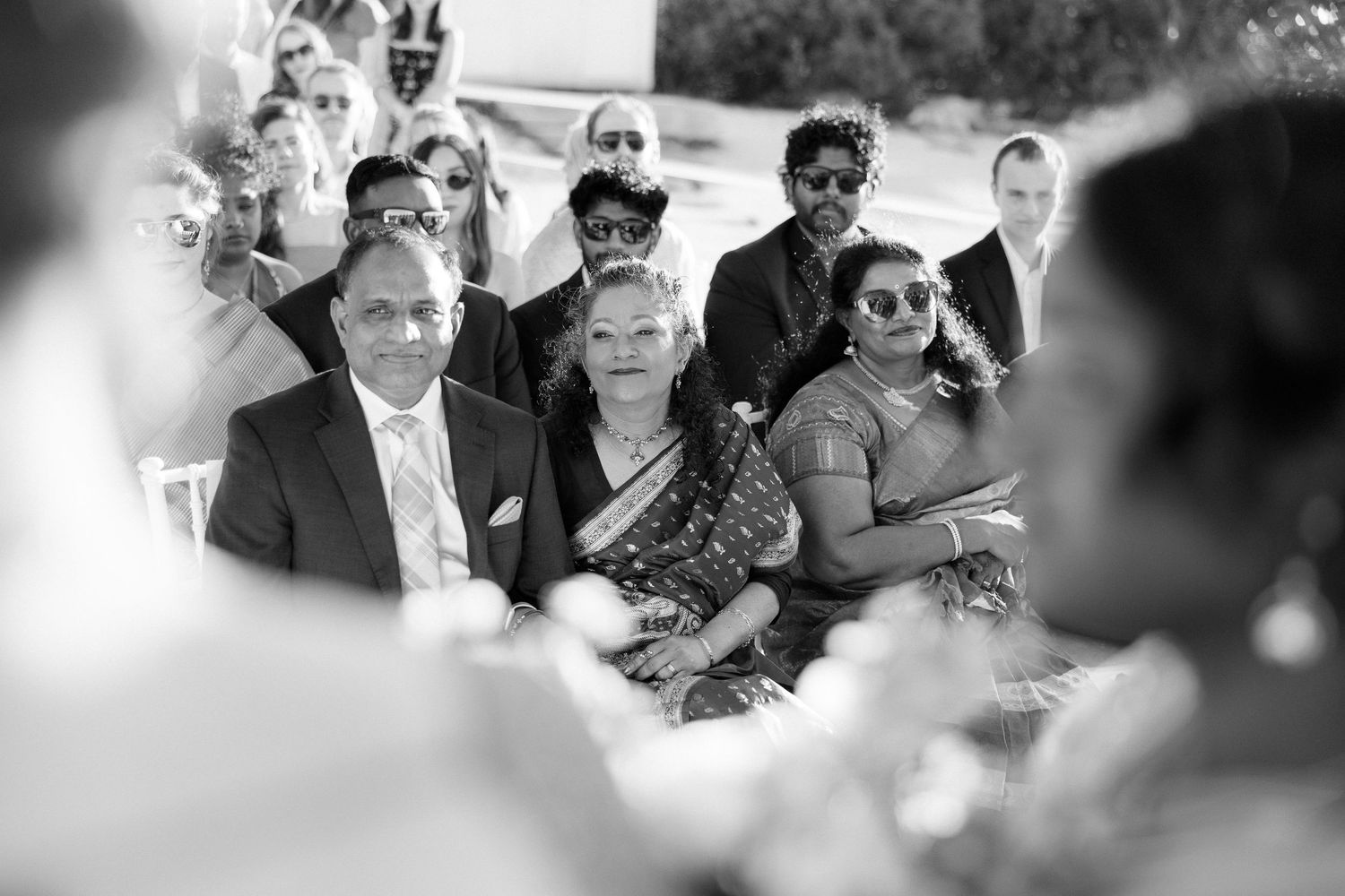 Wedding guests seated outdoors, watching ceremony in black and white photo.
