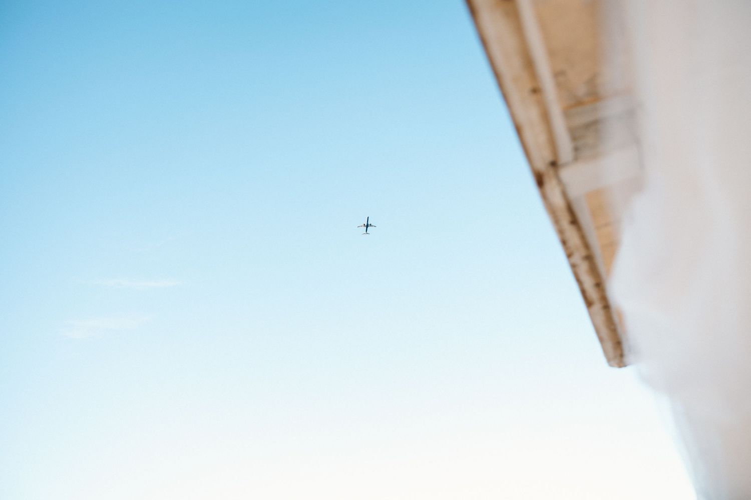 Airplane flying in clear blue sky above corner of white building.
