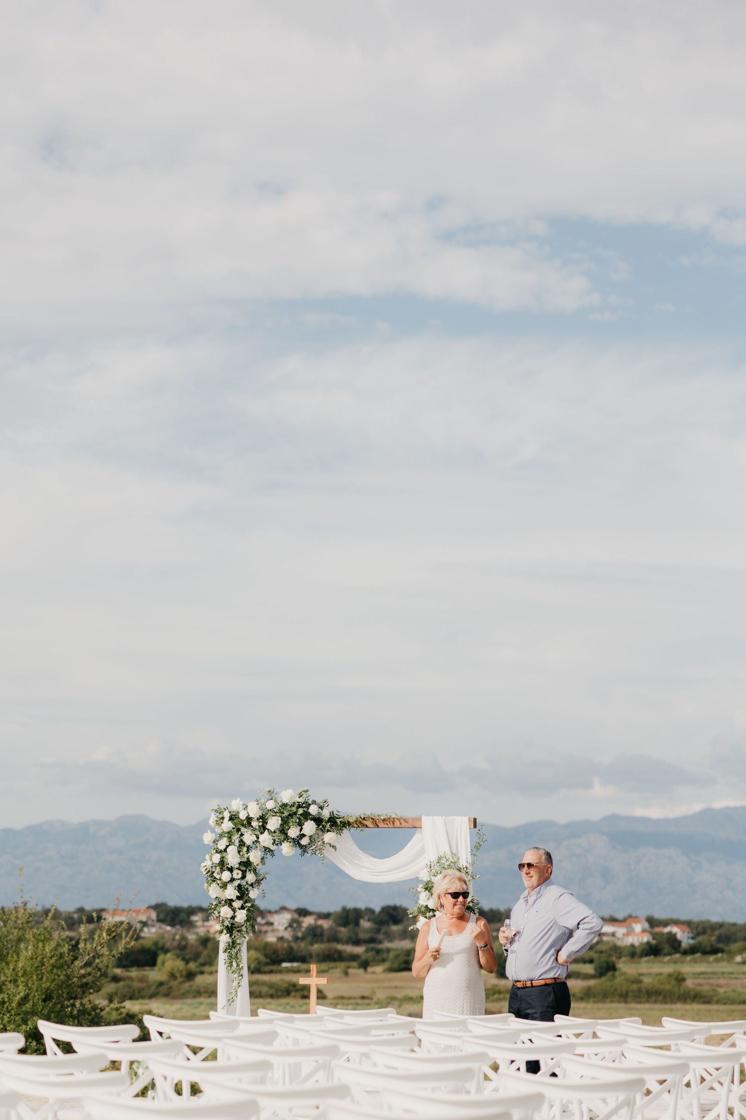 Elegant white table setup with floral arrangements against a mountain backdrop in Italy.