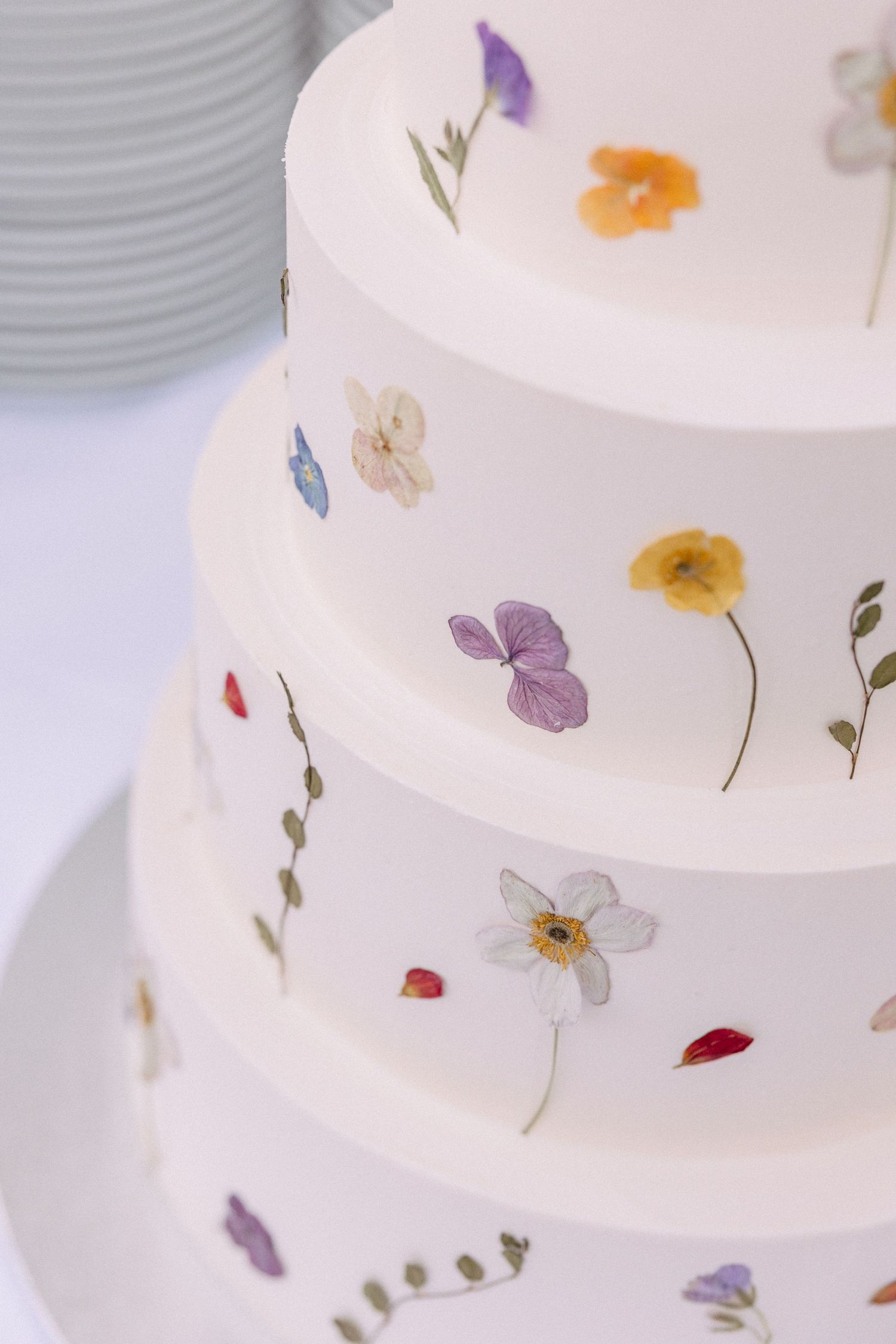 White tiered wedding cake decorated with delicate pressed edible flowers in pastel colors.