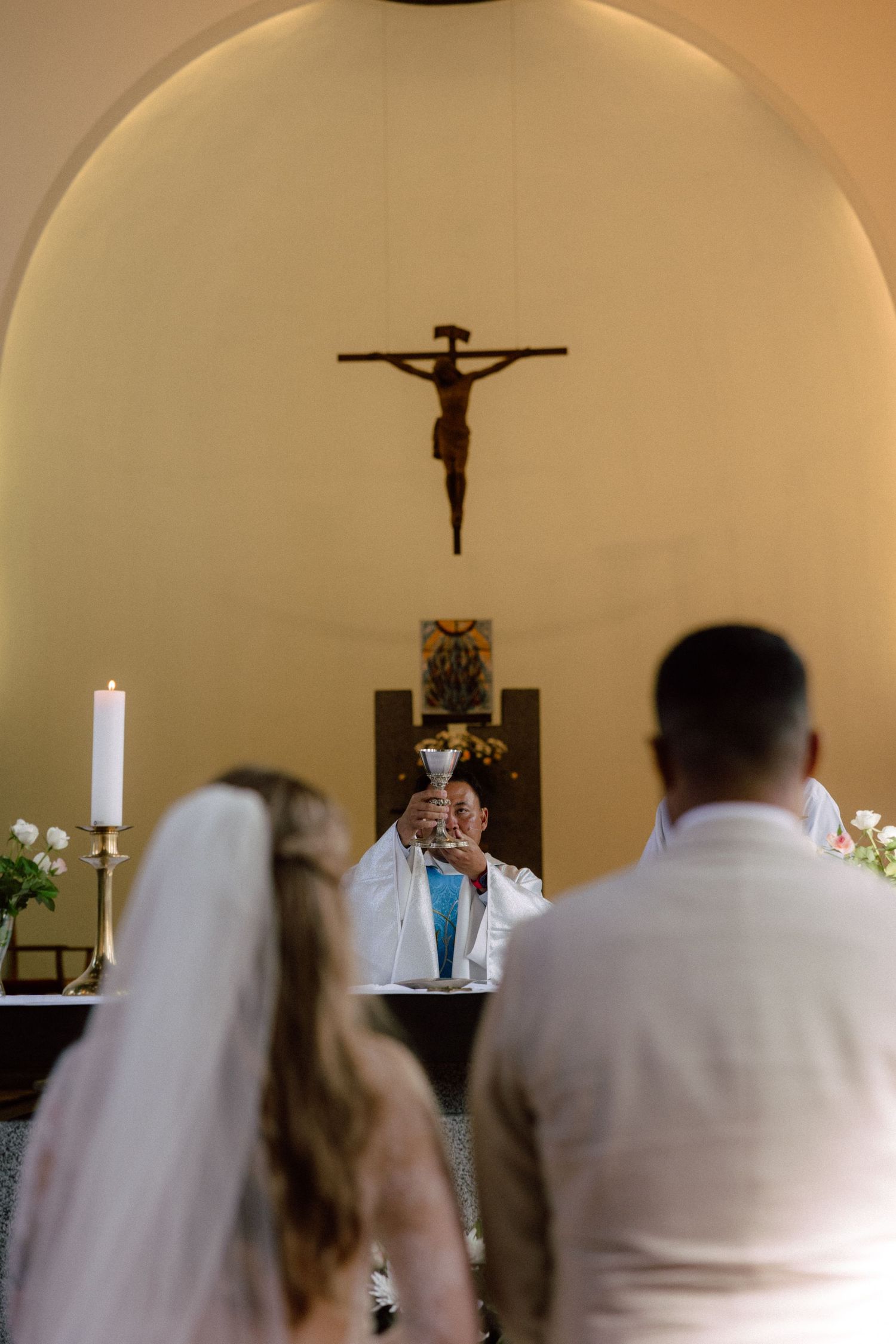 Couple faces altar with crucifix during Catholic wedding ceremony.