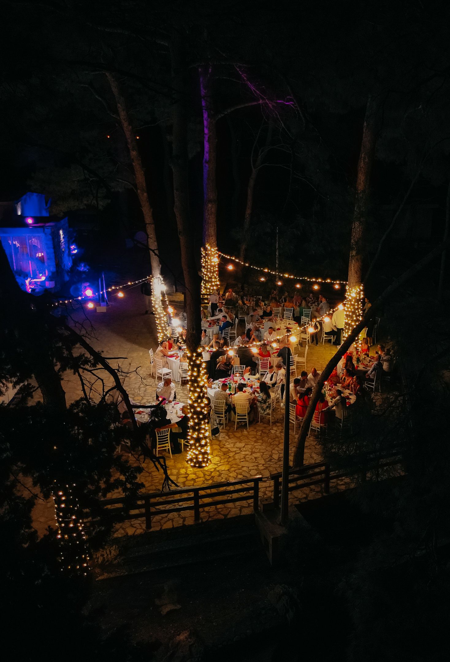 An enchanting outdoor wedding reception at night with string lights illuminating trees and tables under the stars.