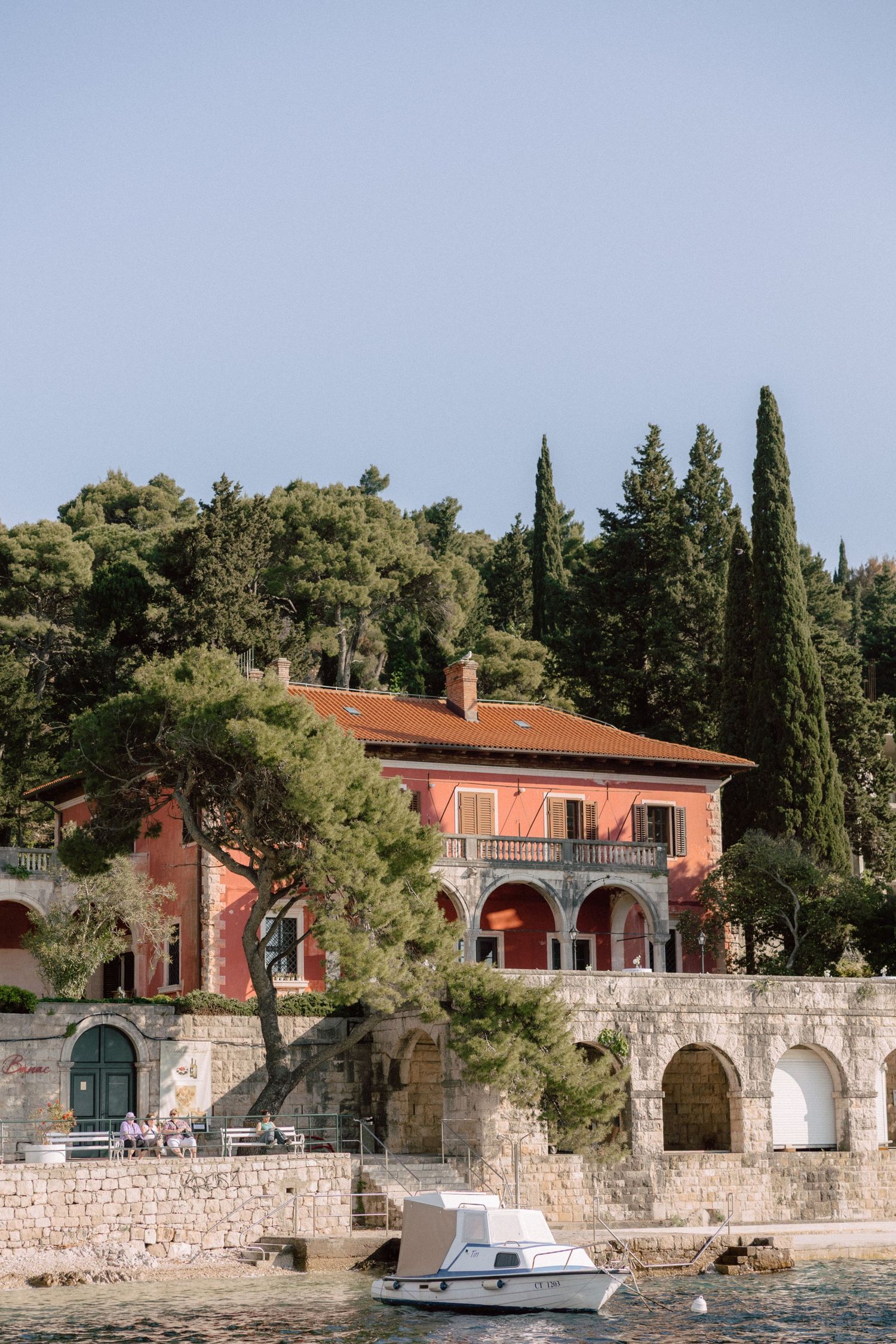 Waterfront Mediterranean villa with terracotta roof and stone walls along the shoreline.