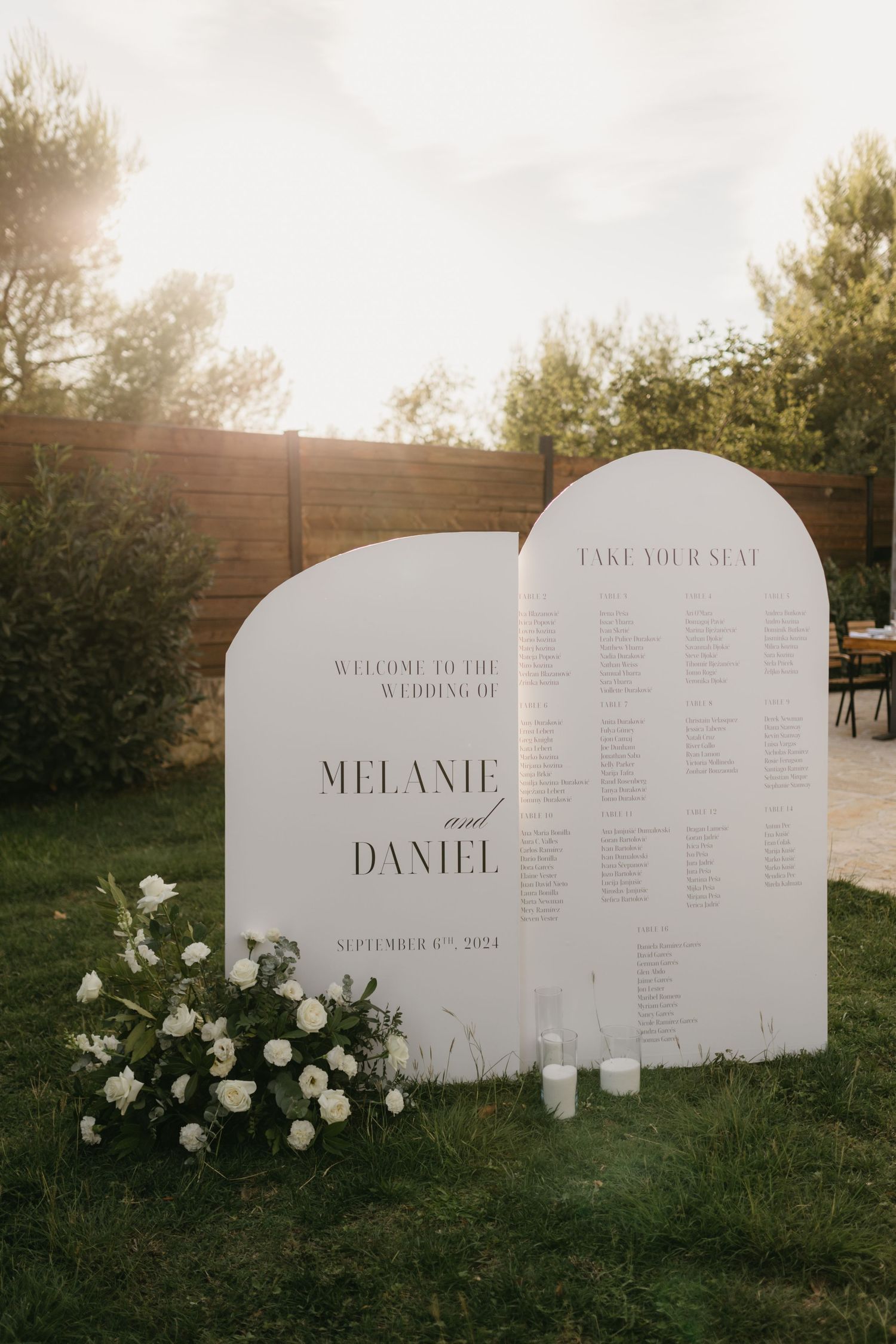 Elegant white curved seating charts with floral decorations display guest names at a wedding venue.