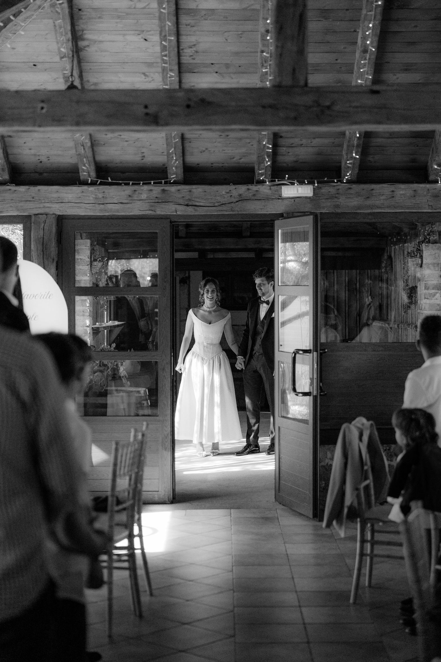 A rustic wooden barn interior with string lights and a white dress displayed.