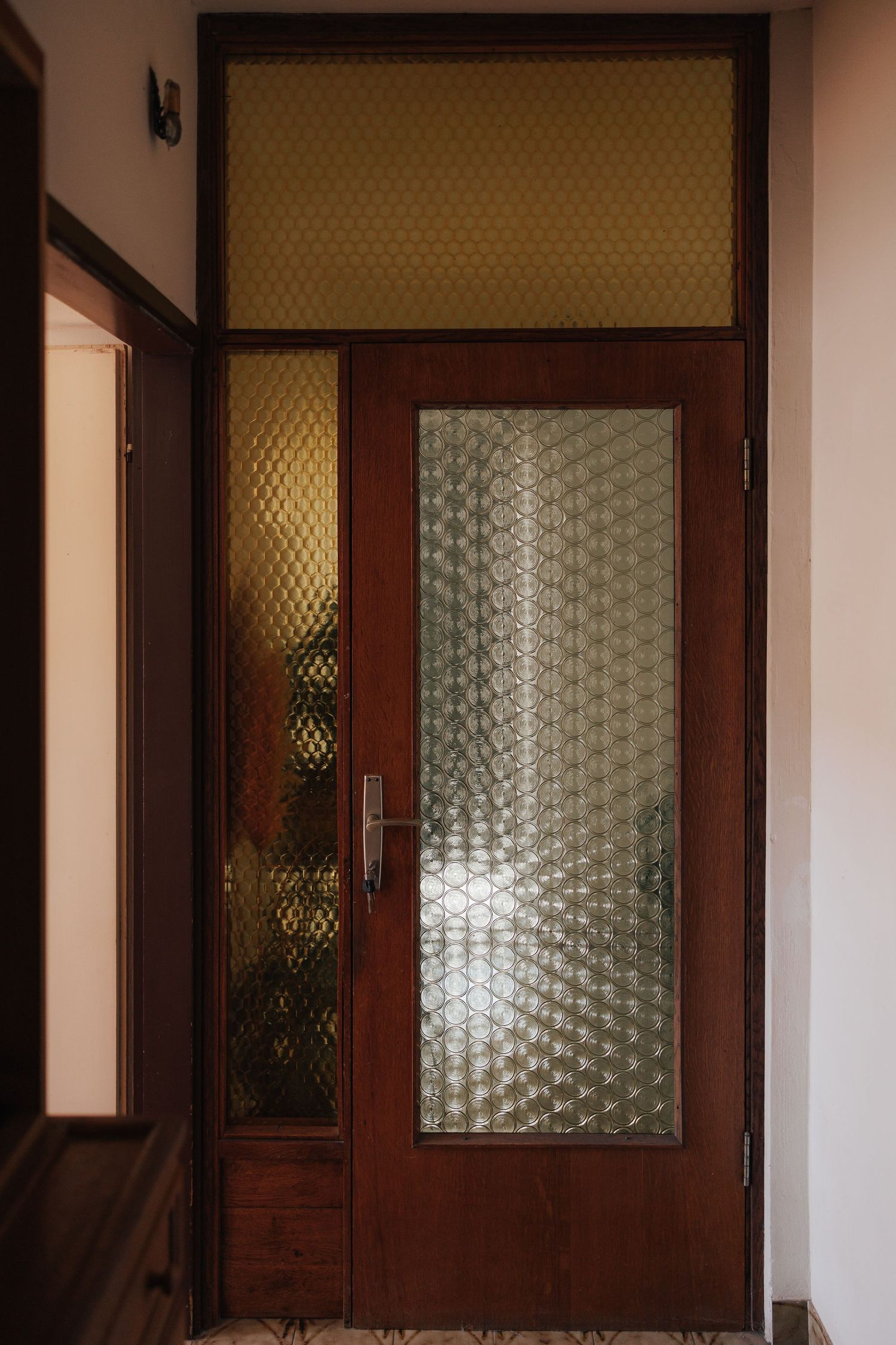 Vintage wooden doors with textured glass panels in a warm-toned hallway.