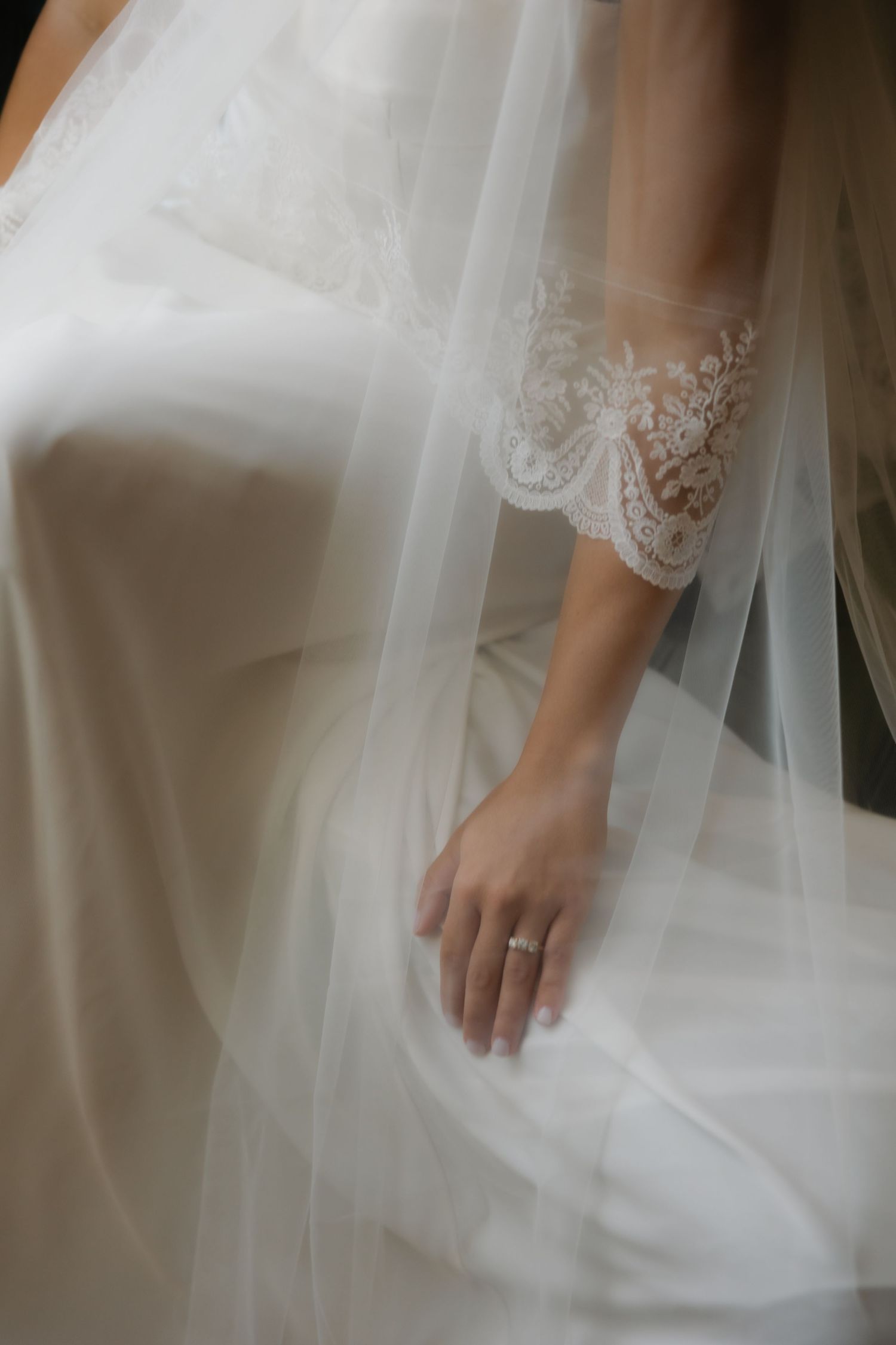 Close-up of bride's hand with diamond ring beneath delicate lace veil.