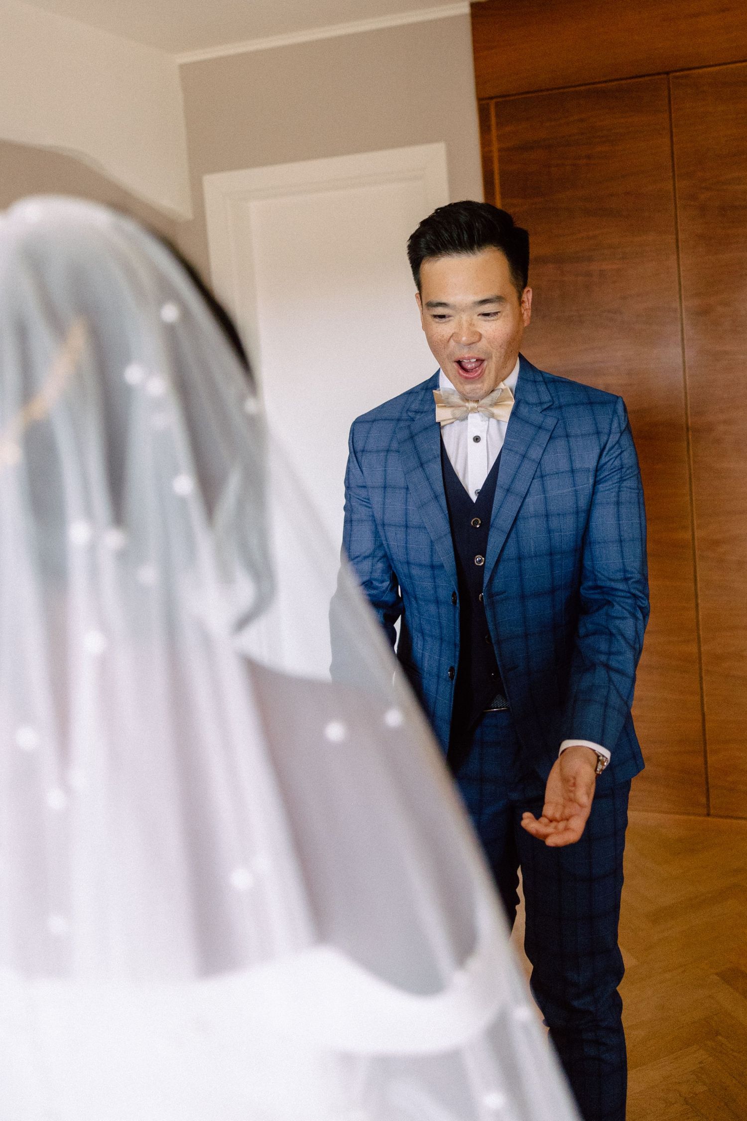 Excited Asian groom in a blue plaid suit reacting with joy upon seeing his veiled bride for the first time.