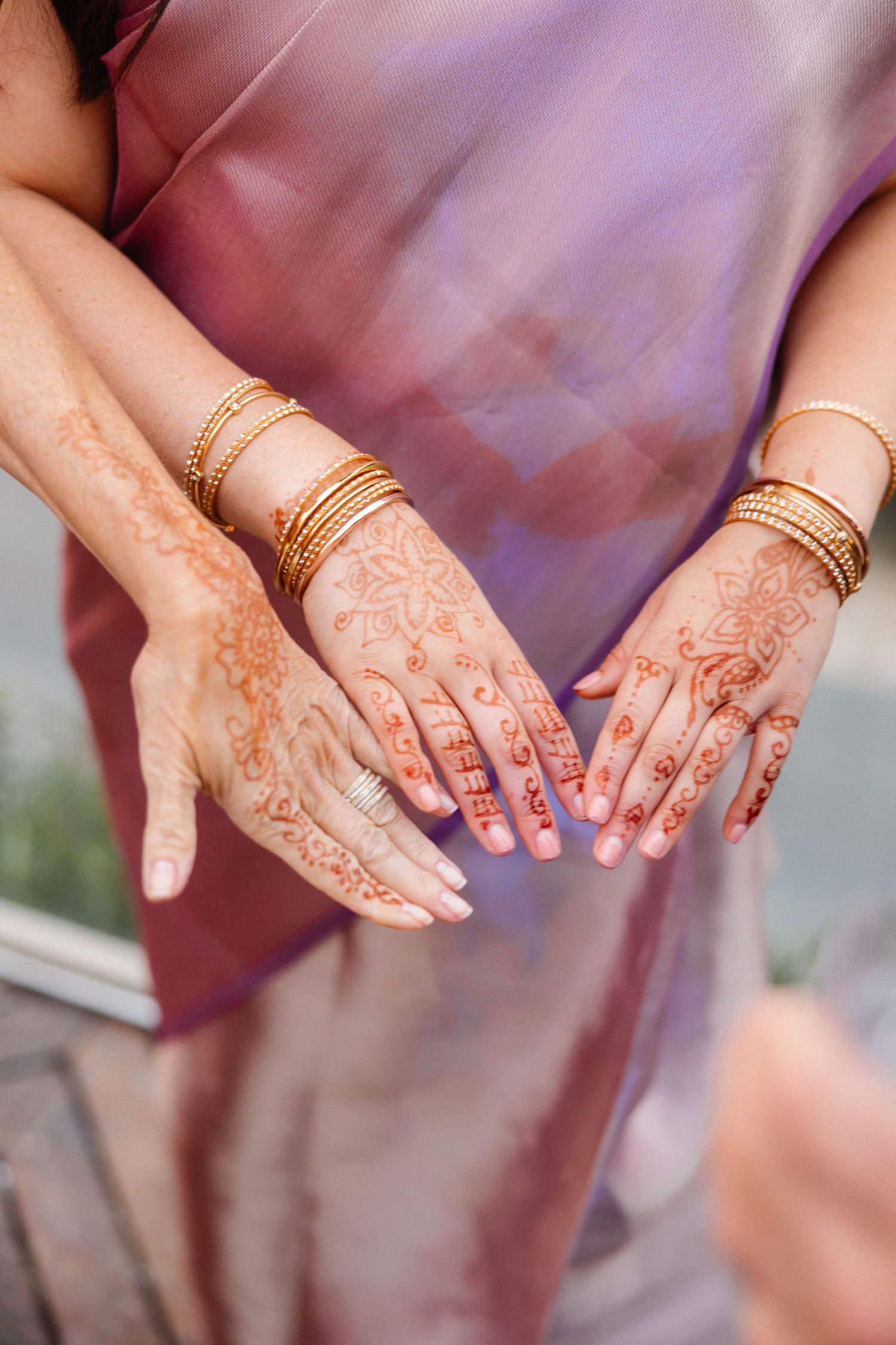 Close-up of hands adorned with intricate henna designs and gold bangles.