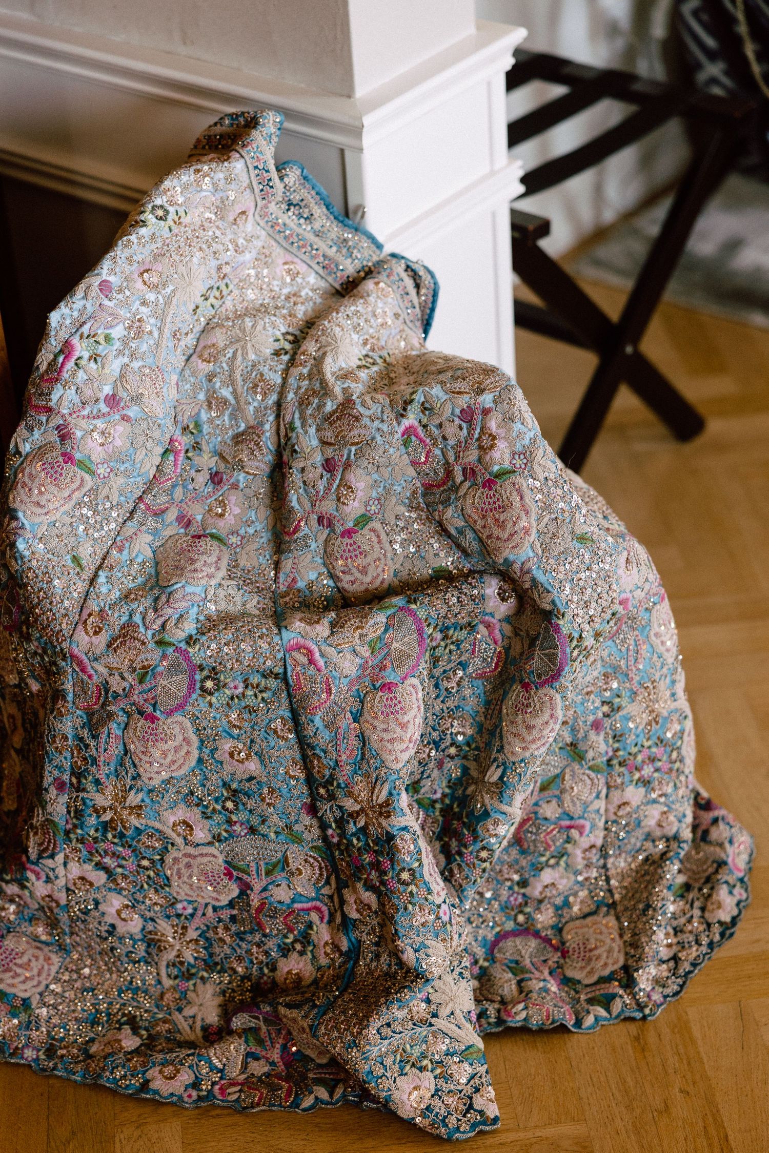 Ornate embroidered bridal lehenga with intricate floral patterns and sequins draped over a chair.