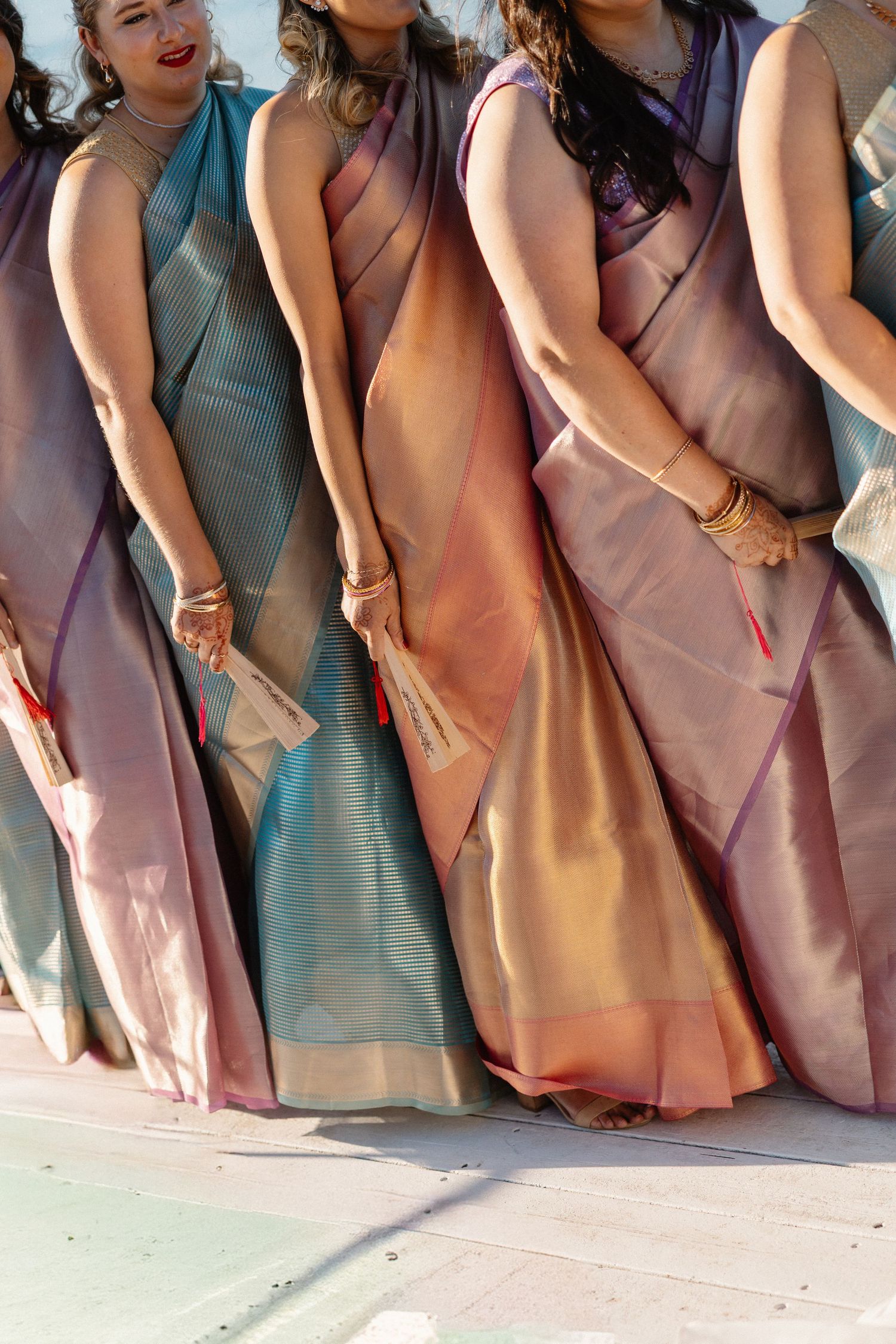 Group of women wearing colorful silk sarees in pink, blue, and gold at an outdoor wedding ceremony.