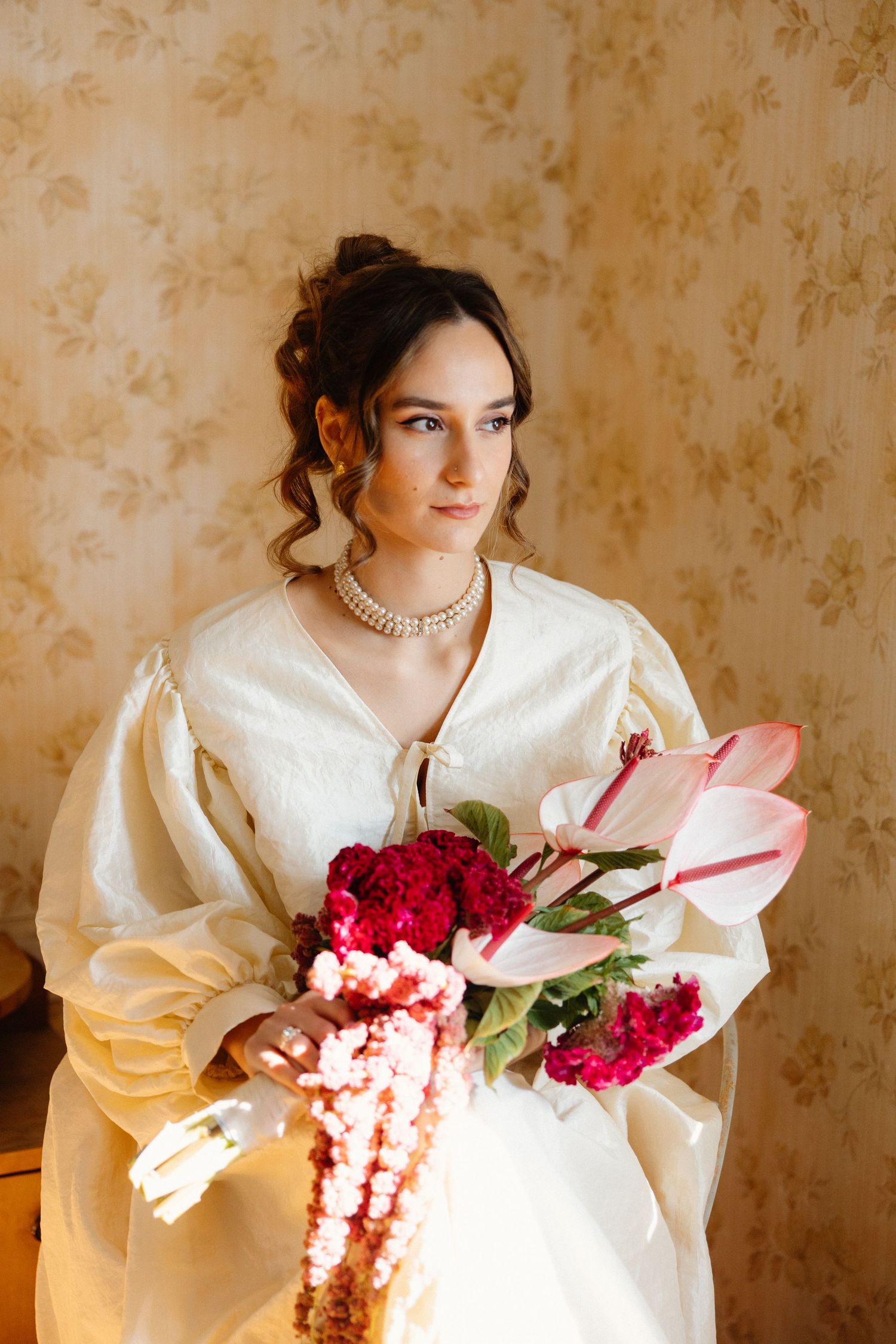 Cream-colored vintage dress with red floral bouquet against floral wallpaper.