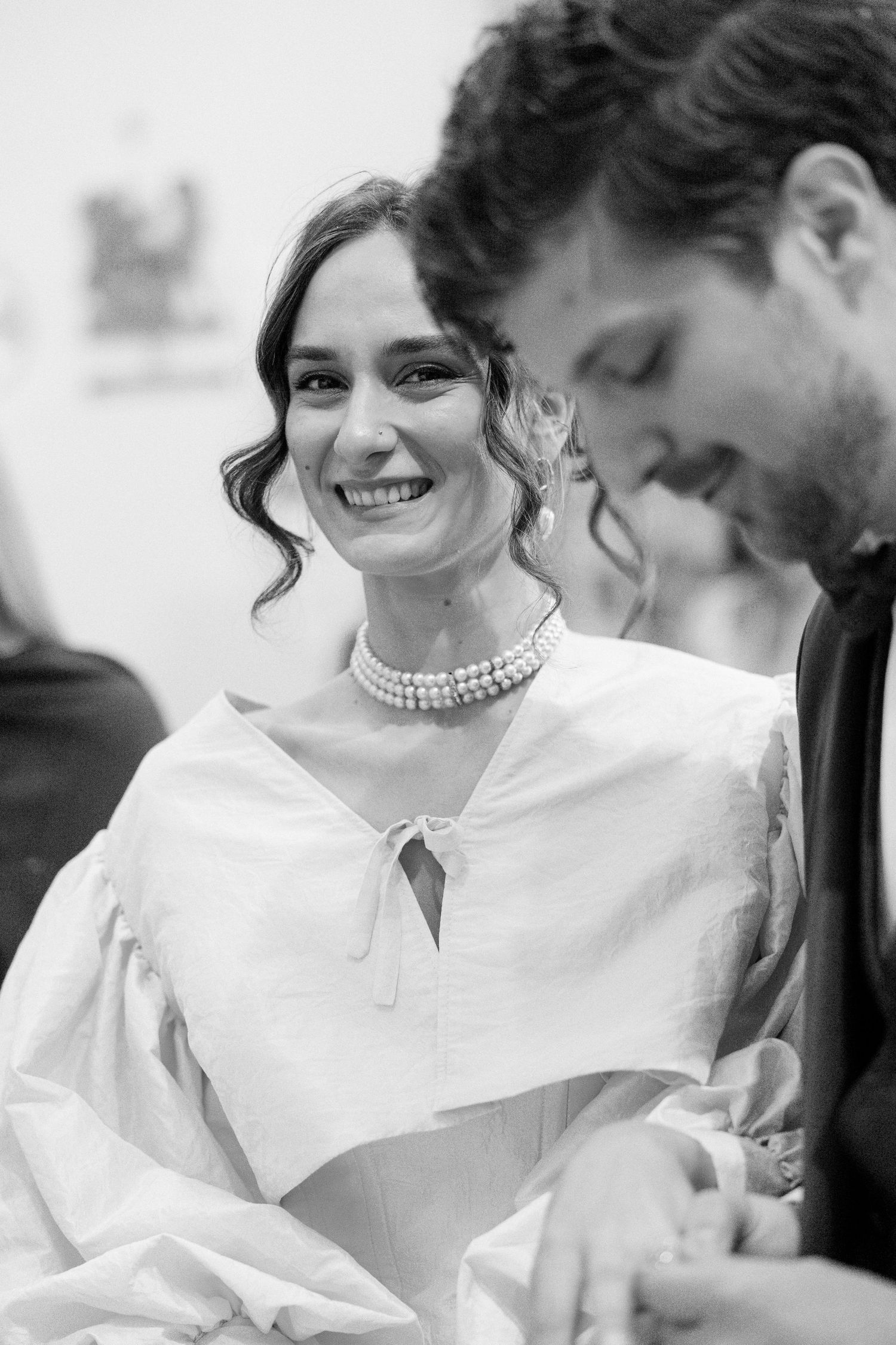 A black and white portrait showing a pearl necklace and elegant white dress with puffed sleeves.