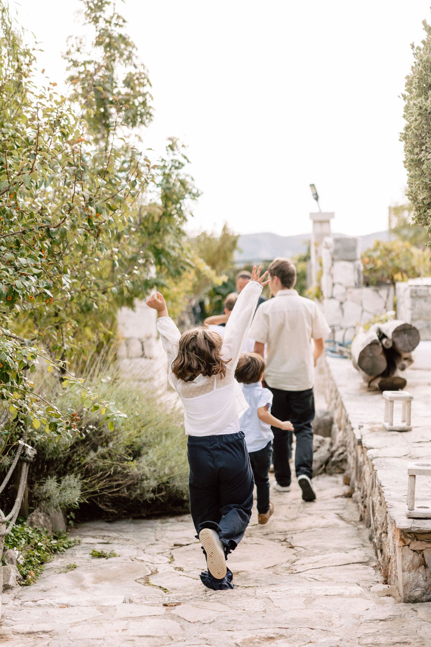 Wedding guests sitting along a stone wall in a Mediterranean garden setting.
