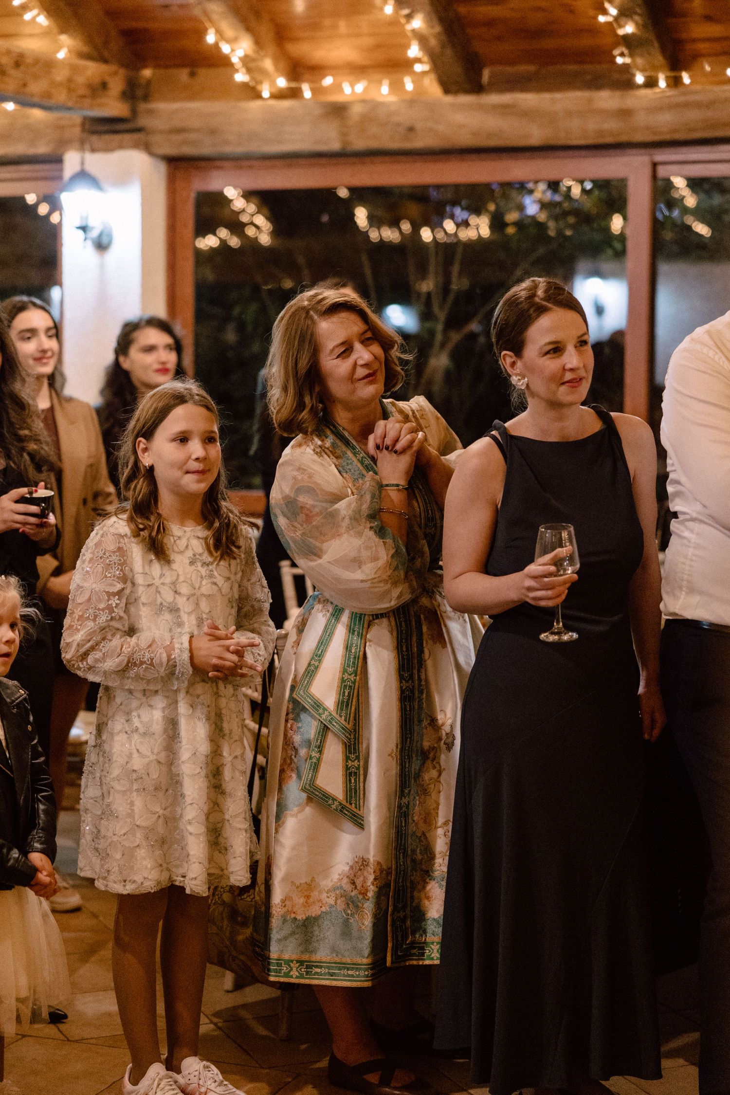 Wedding reception guests mingling under string lights in rustic venue.