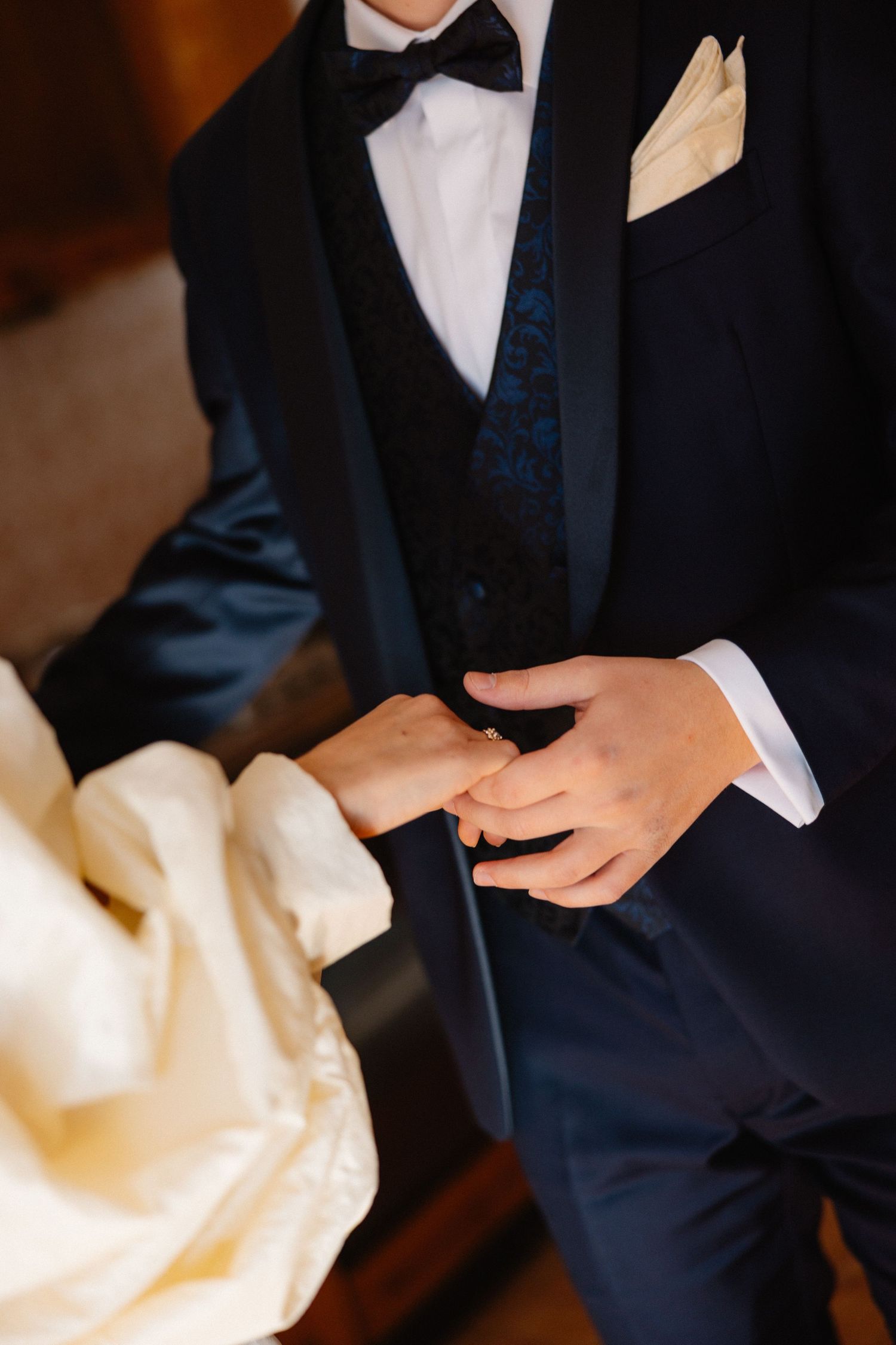 Close-up of hands in formal attire with white shirt cuffs and navy suit jacket.