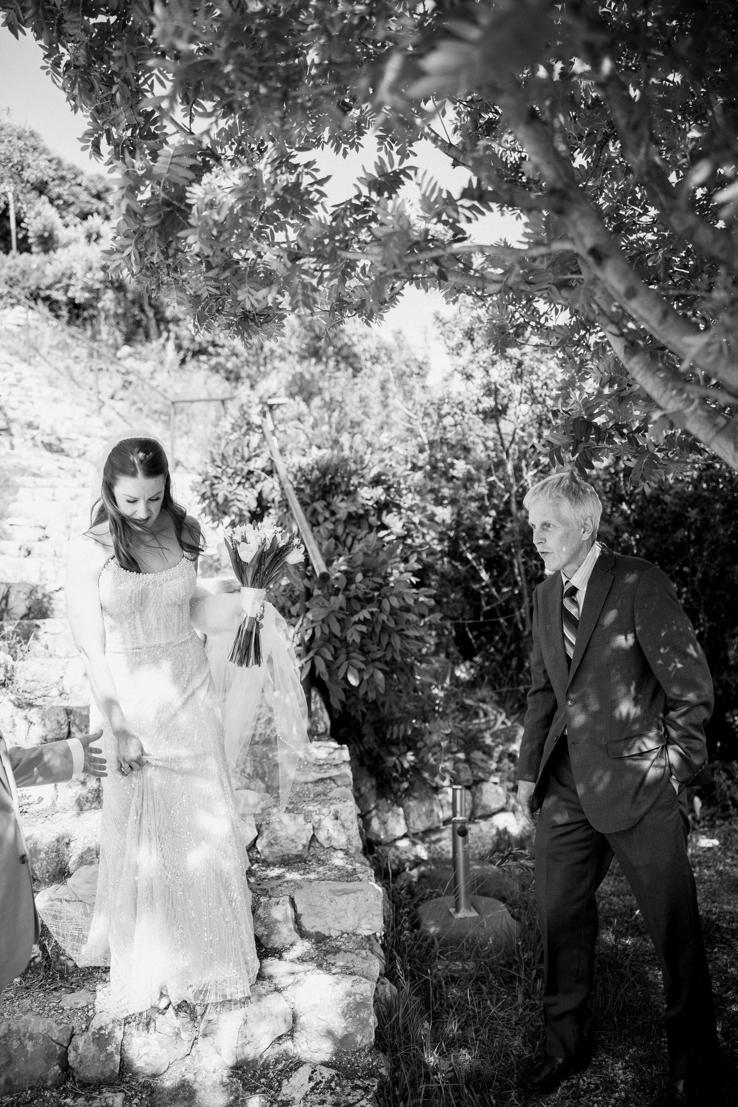 Black and white wedding portrait taken under trees with soft natural light filtering through the leaves.