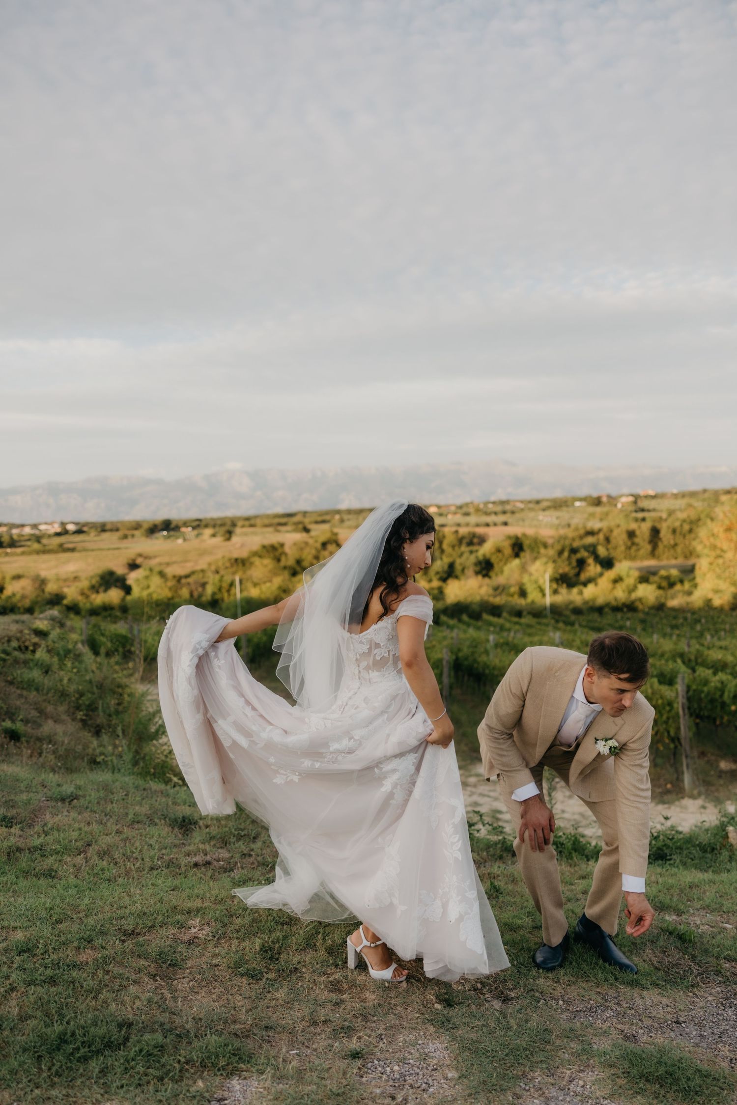 A couple in wedding attire walks along a countryside path during golden hour.