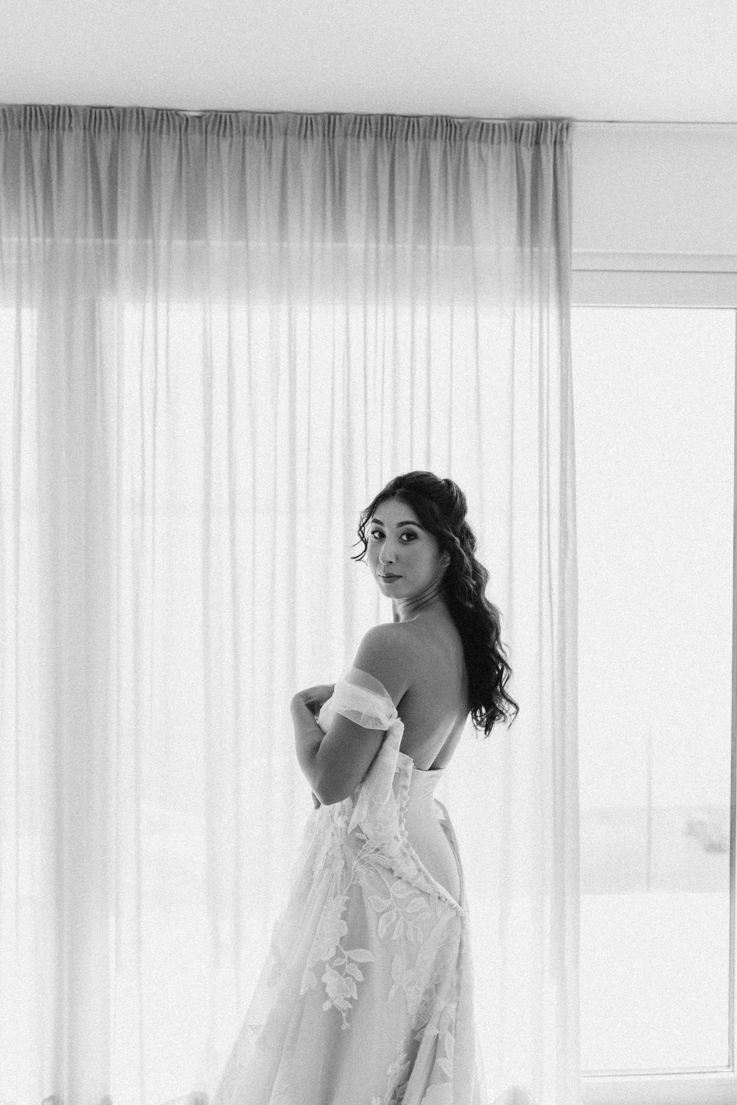 Ethereal bridal boudoir session with white lace robe and sheer curtains.