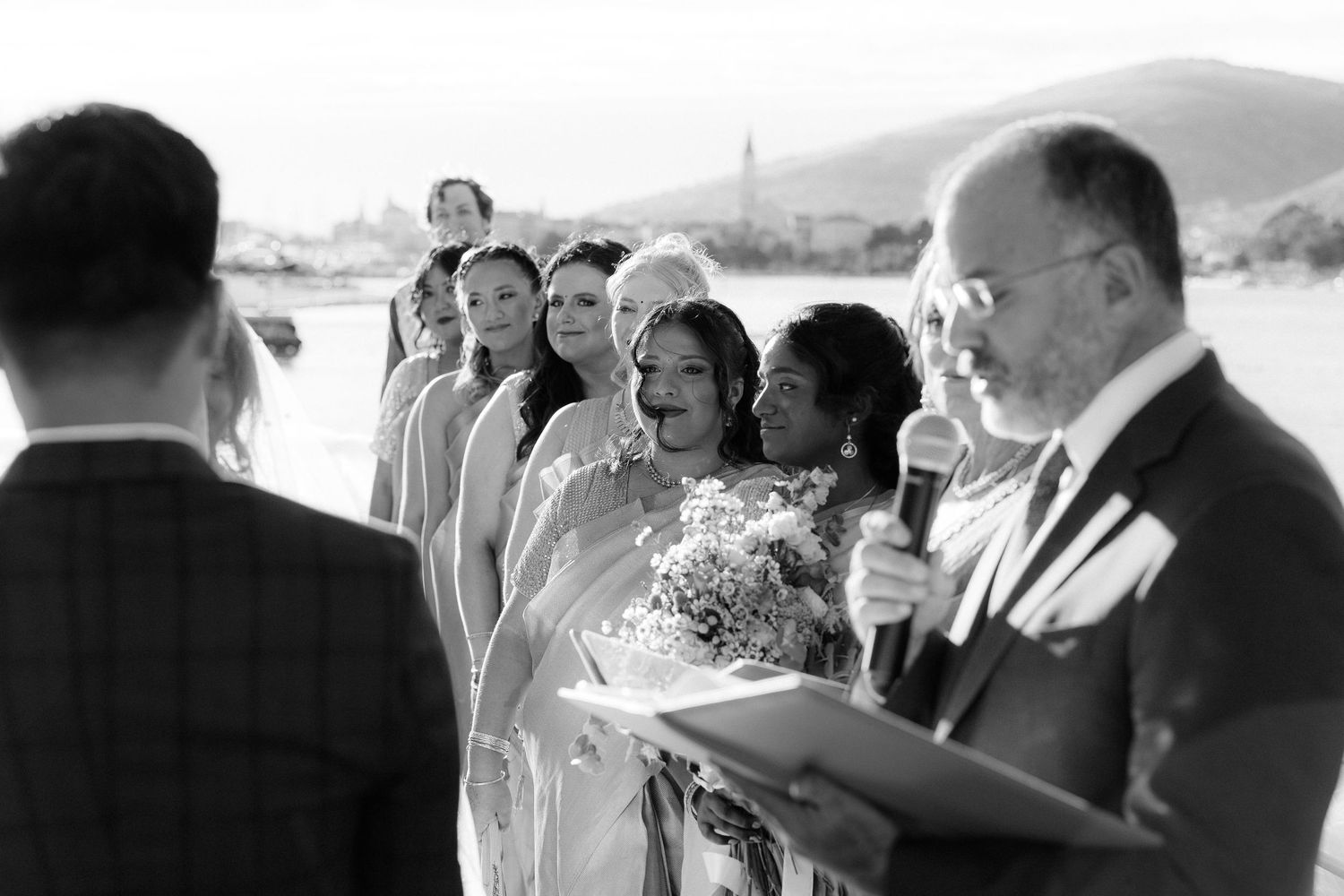 Black and white photo of emotional bride at altar surrounded by bridesmaids during outdoor ceremony.