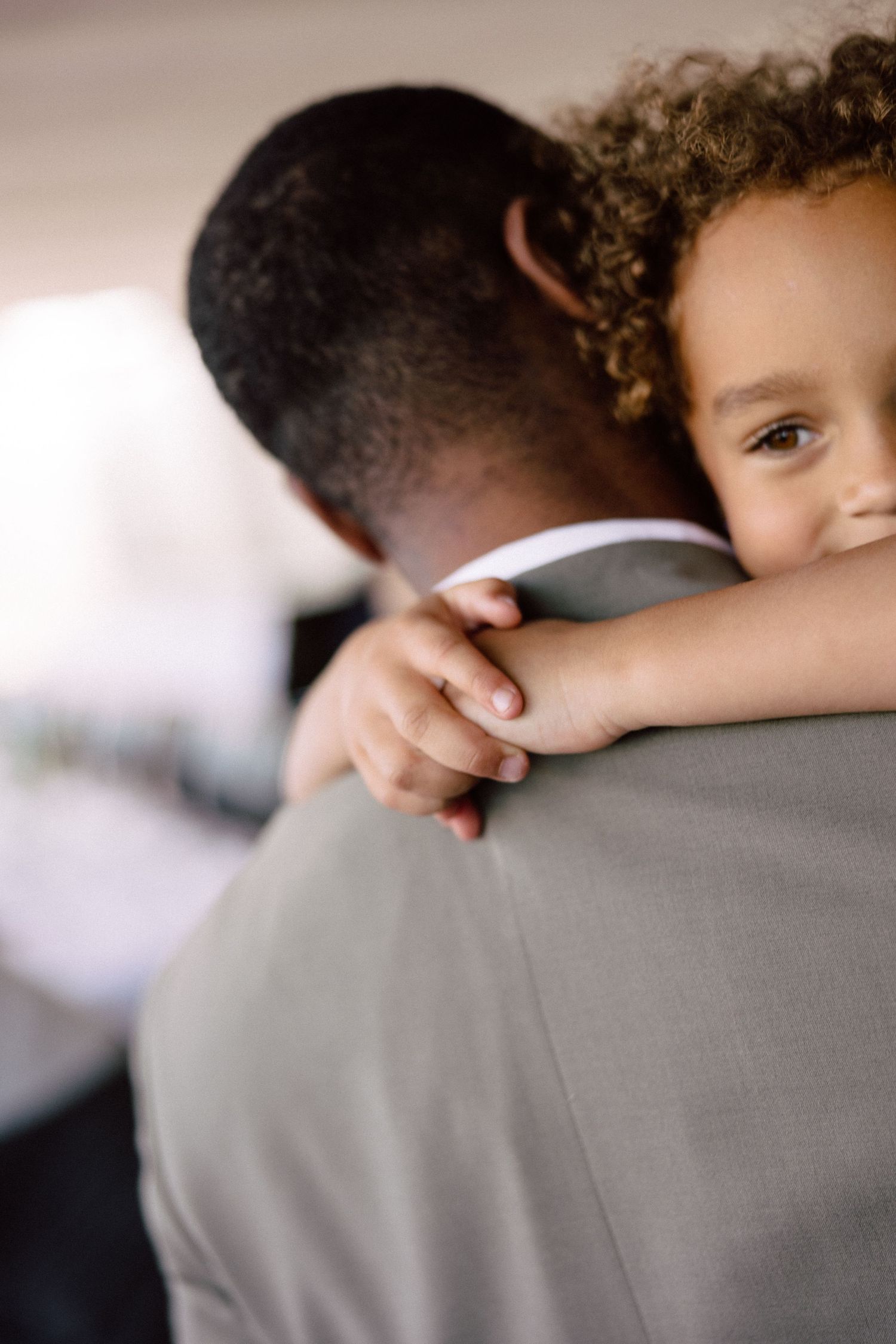 A tender moment captured as a small child with curly hair hugs someone in formal attire.