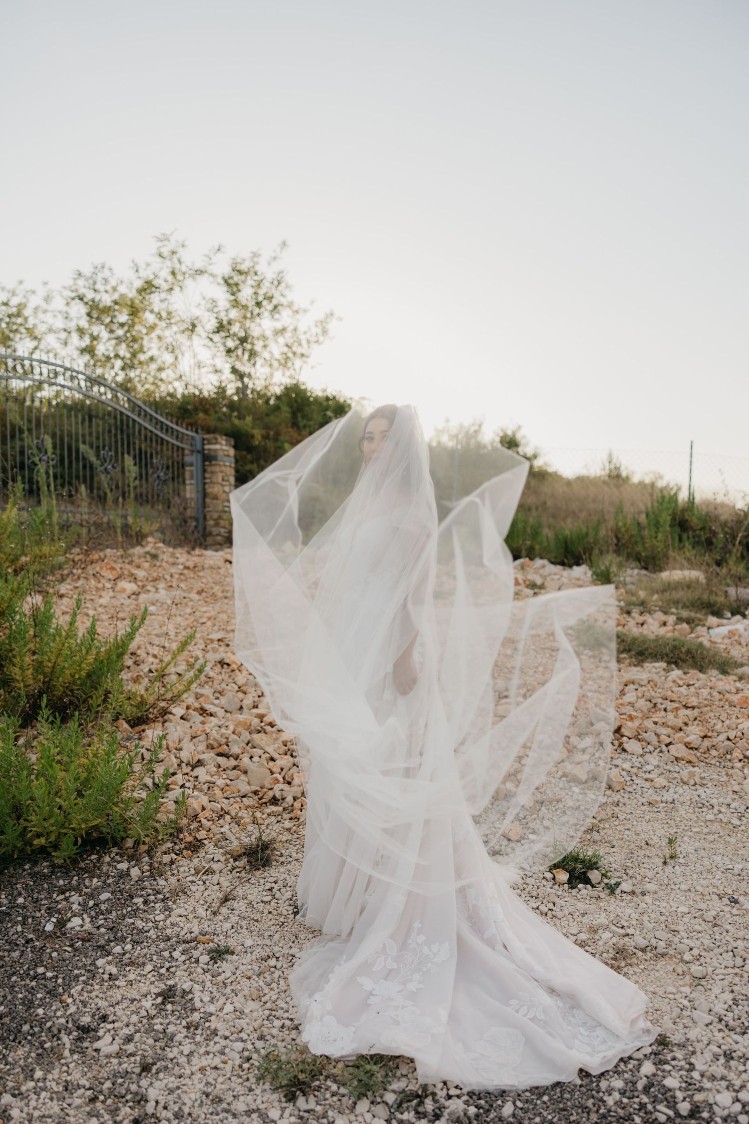 Flowing white wedding veil catches wind dramatically on rocky terrain.
