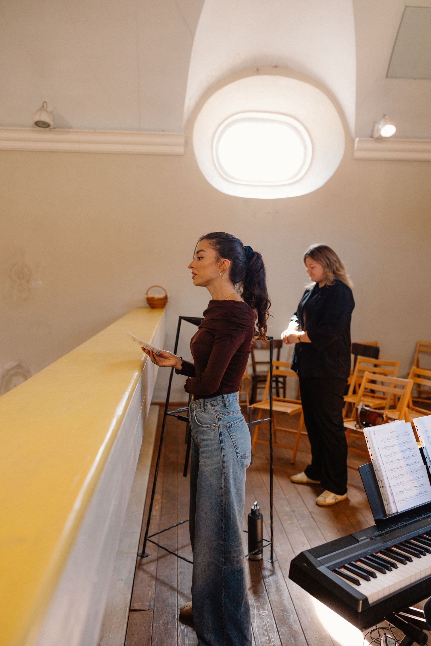 Musicians rehearse in a bright studio space with a piano and music stands.
