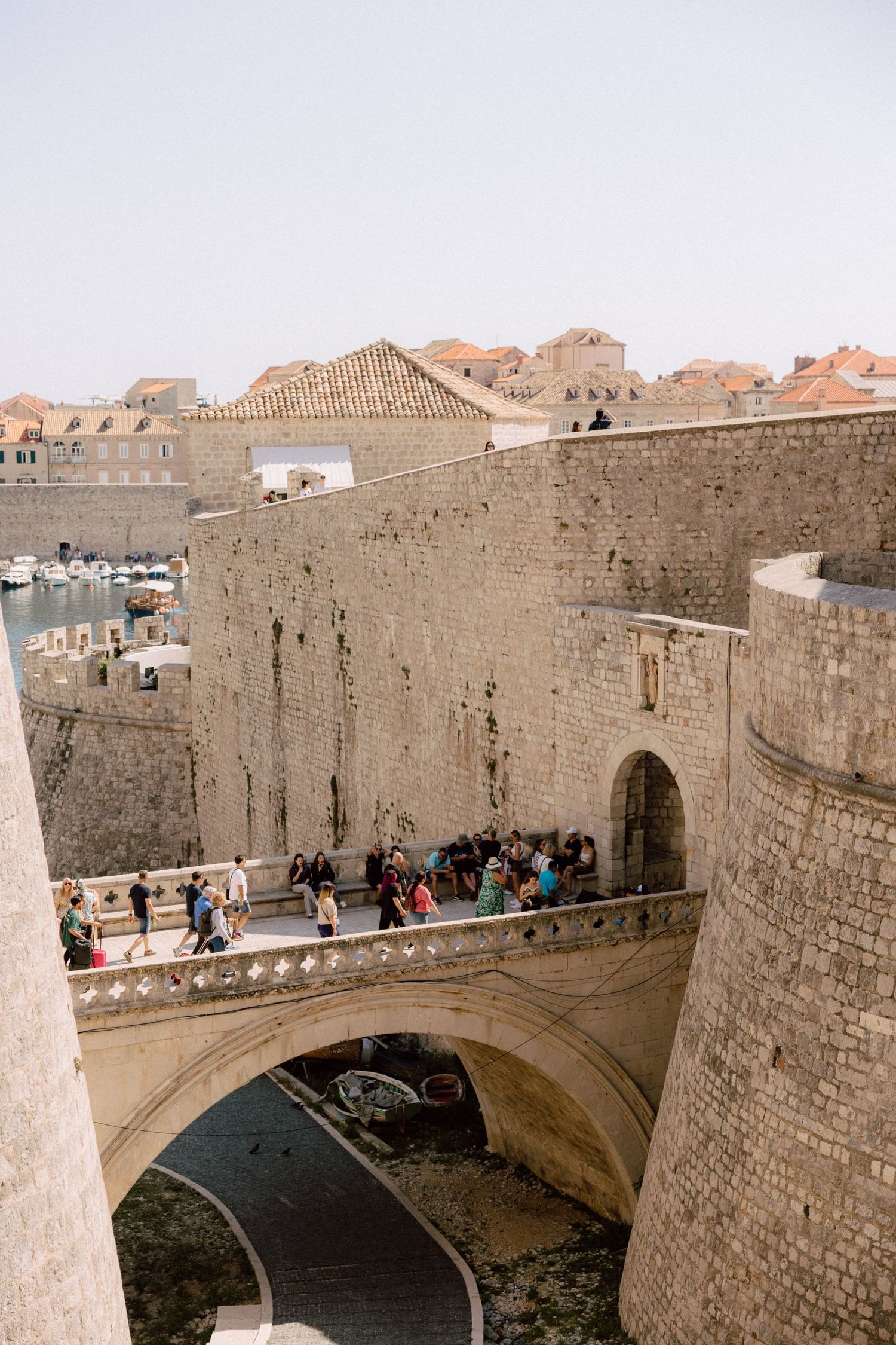 Ancient stone city walls and archway bridge with tourists walking along the fortification.