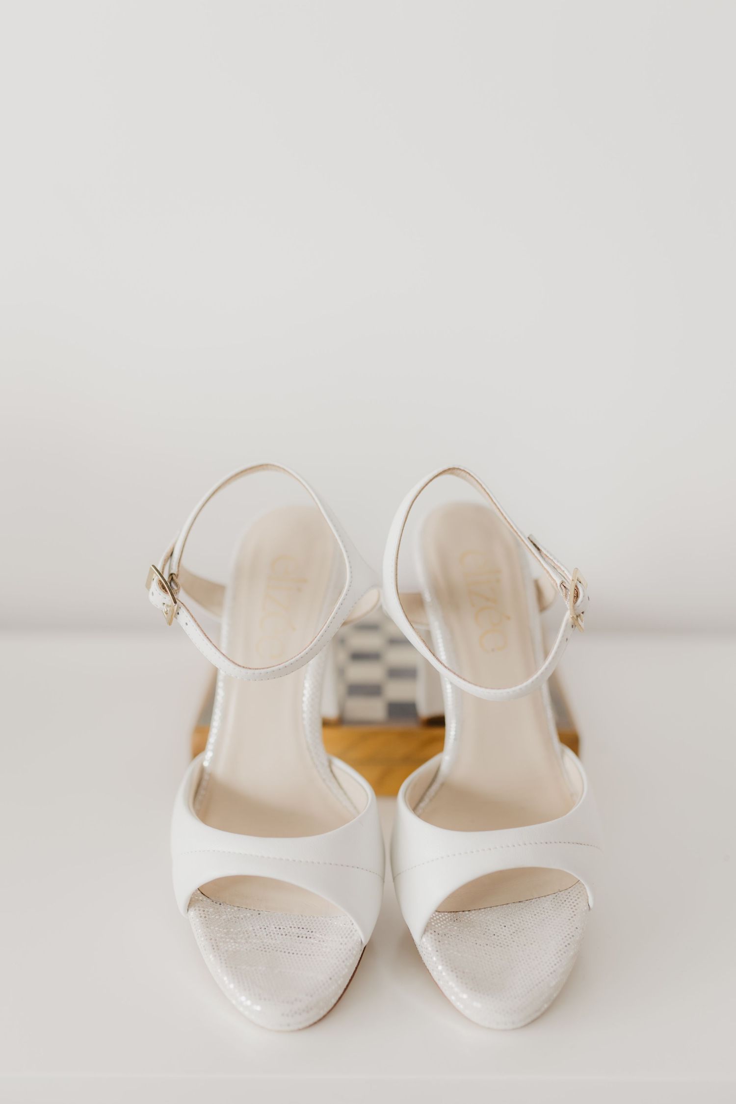 Elegant white bridal sandals with ankle straps on light background.