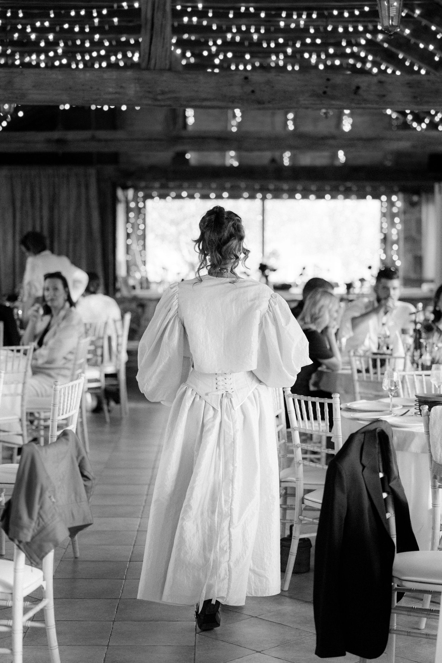 Wedding reception venue with white chairs and string lights hanging from wooden beams.