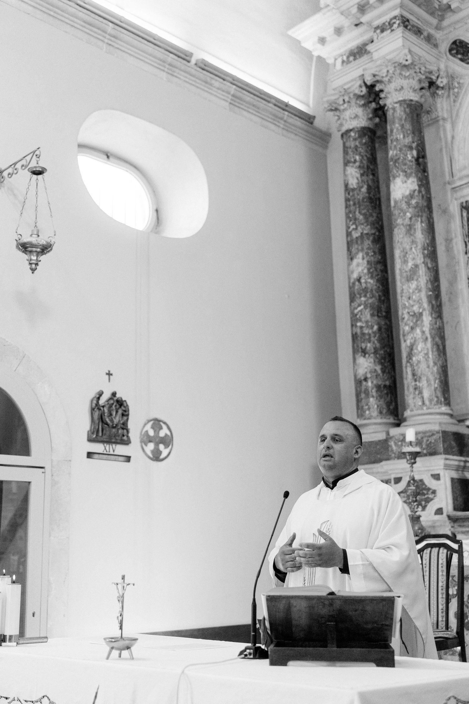 Interior of ornate church with marble columns and arched windows during religious service.