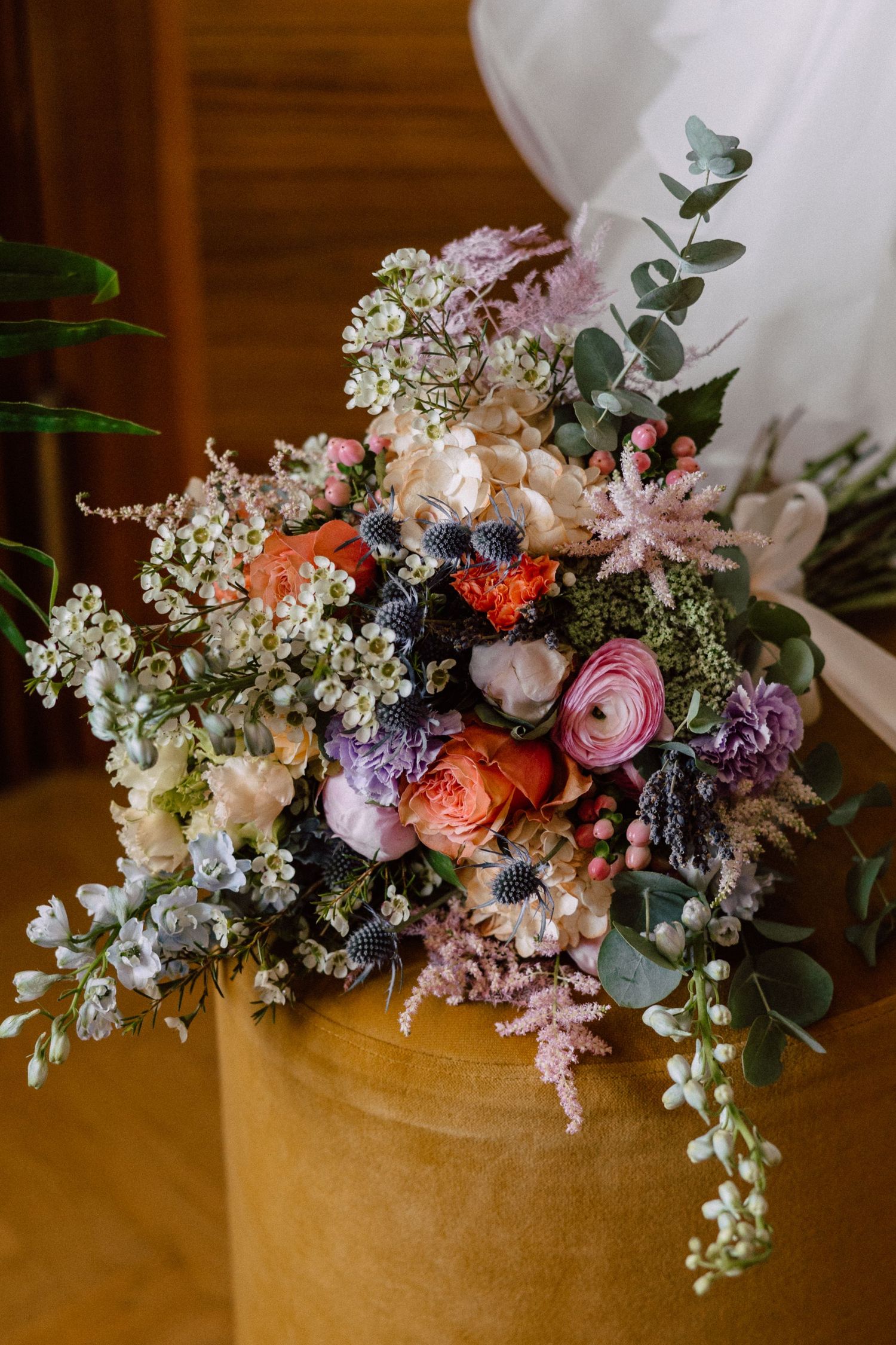 Lush bridal bouquet featuring ranunculus, thistle, eucalyptus, and wildflowers in pink, orange, and white tones.