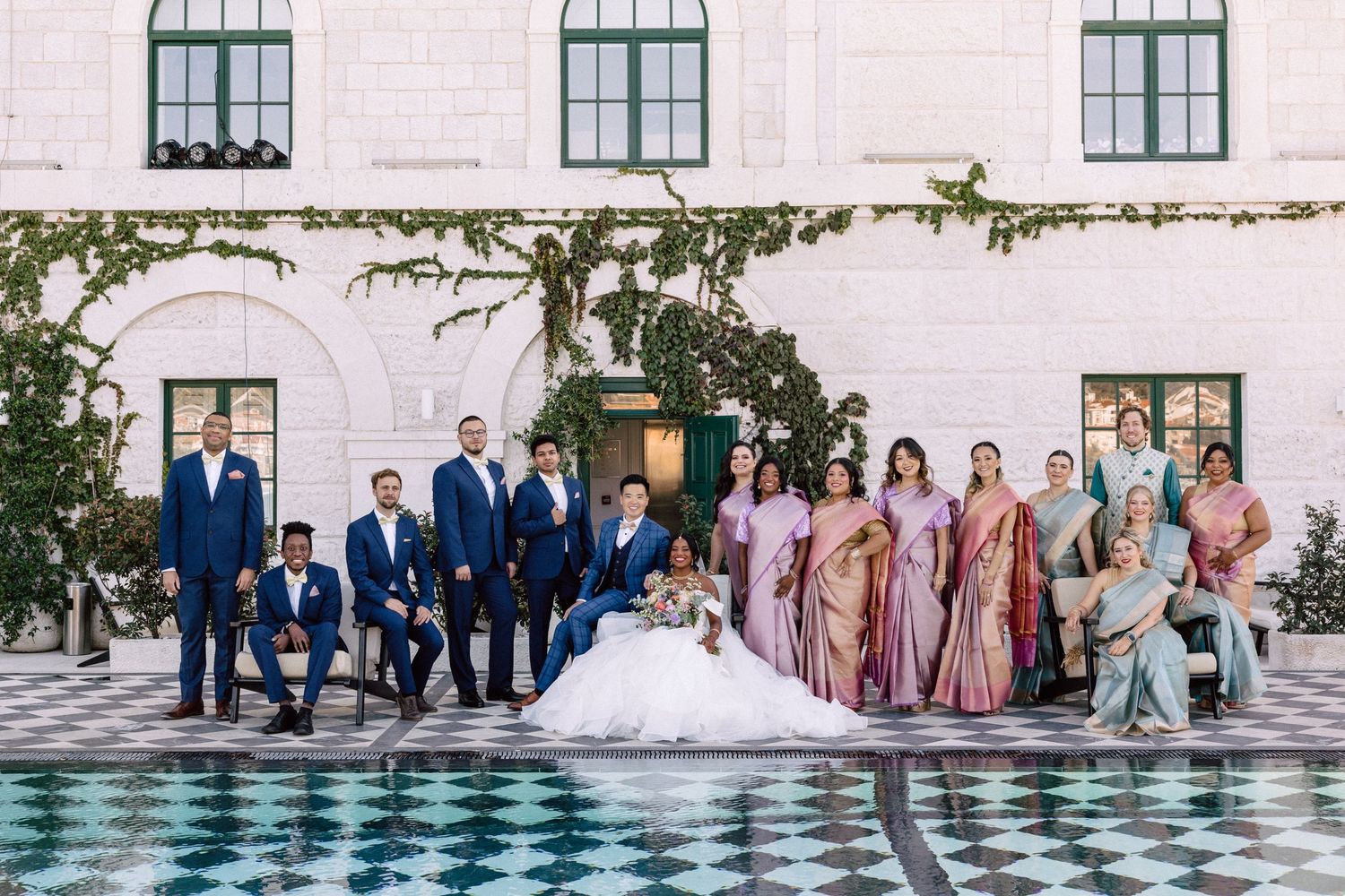 Wedding party posing outdoors with groomsmen in blue suits and bridesmaids in pink silk sarees.