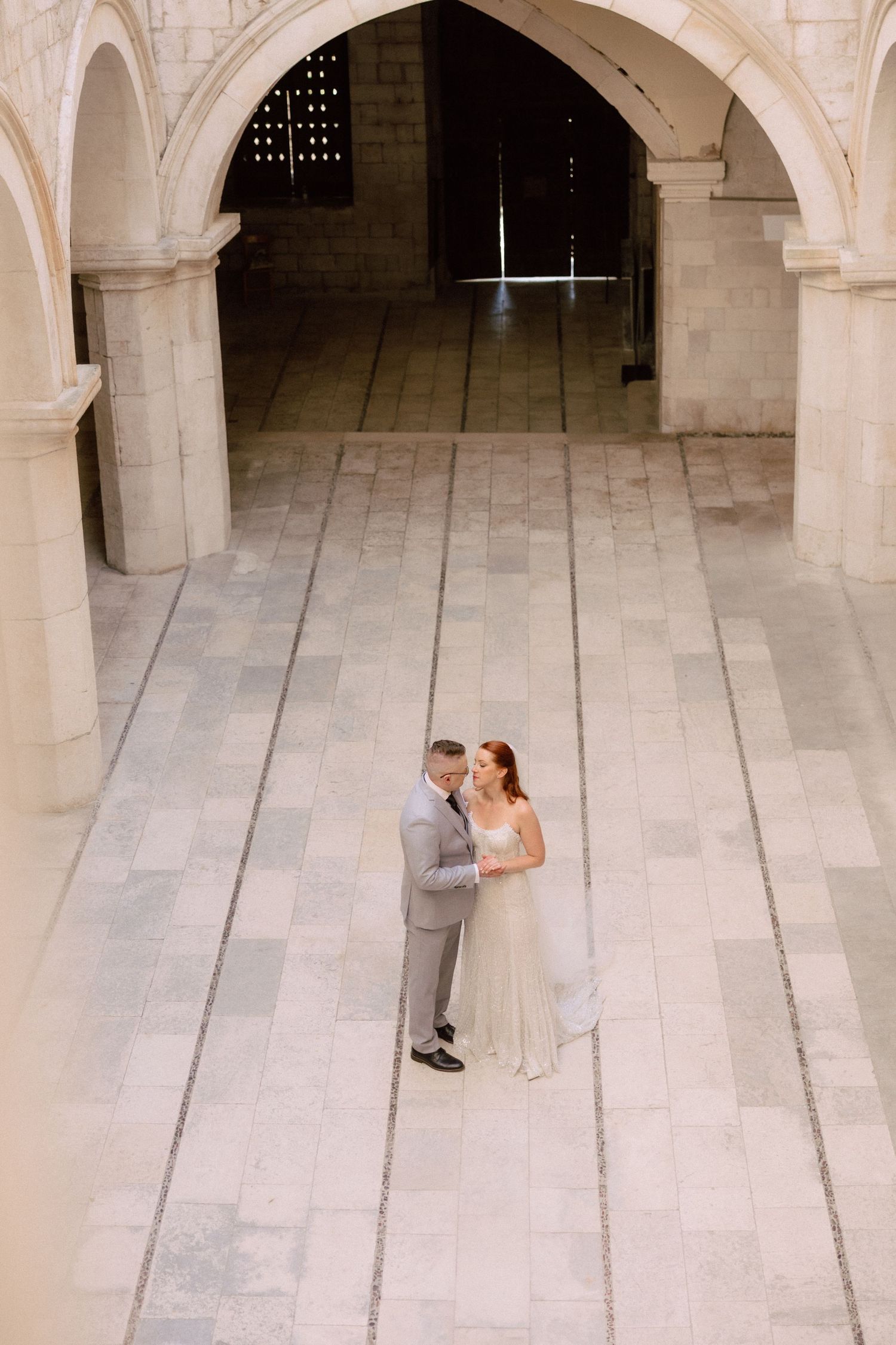 Wedding couple dancing in a historic stone courtyard with elegant archways  in Dubrovnik, Croatia.