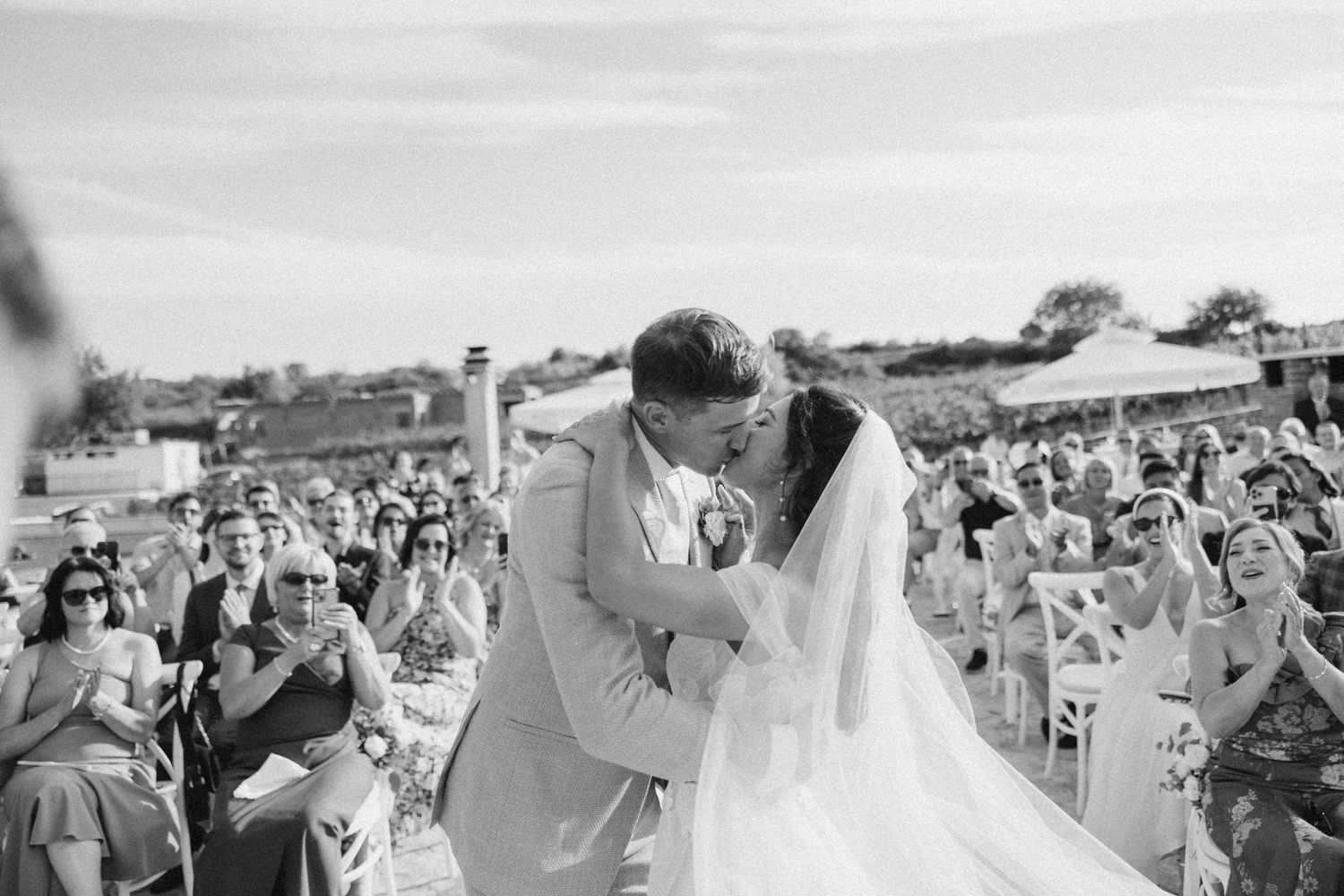 Wide shots of wedding guests watching an outdoor ceremony against a cloudy sky in Italy.