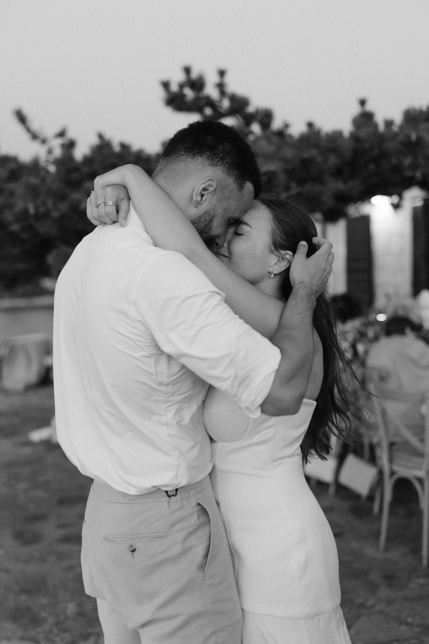 Black and white photo of bride and groom sharing tender embrace at outdoor wedding reception.