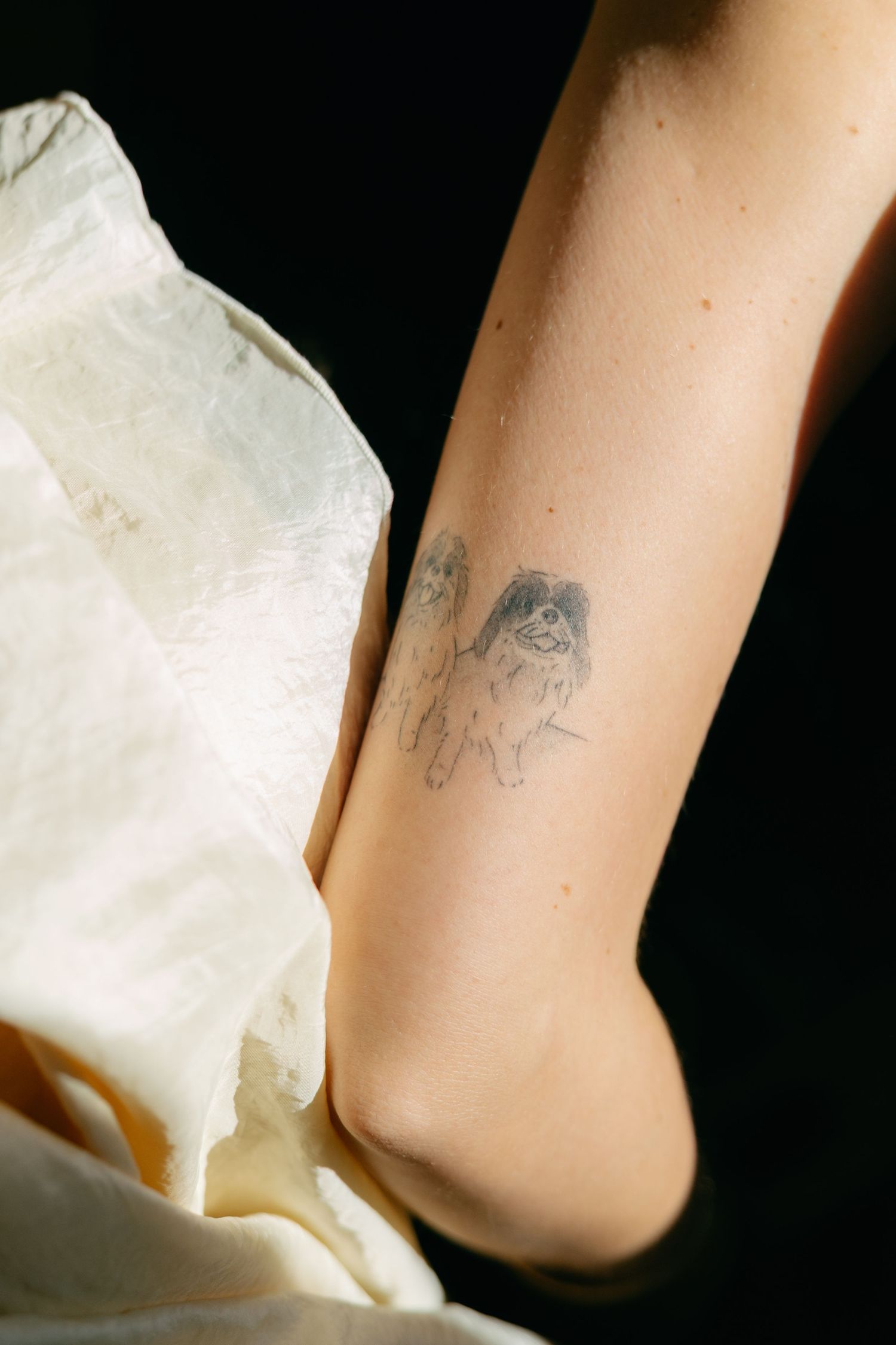 Small delicate tattoo on arm against white fabric background.