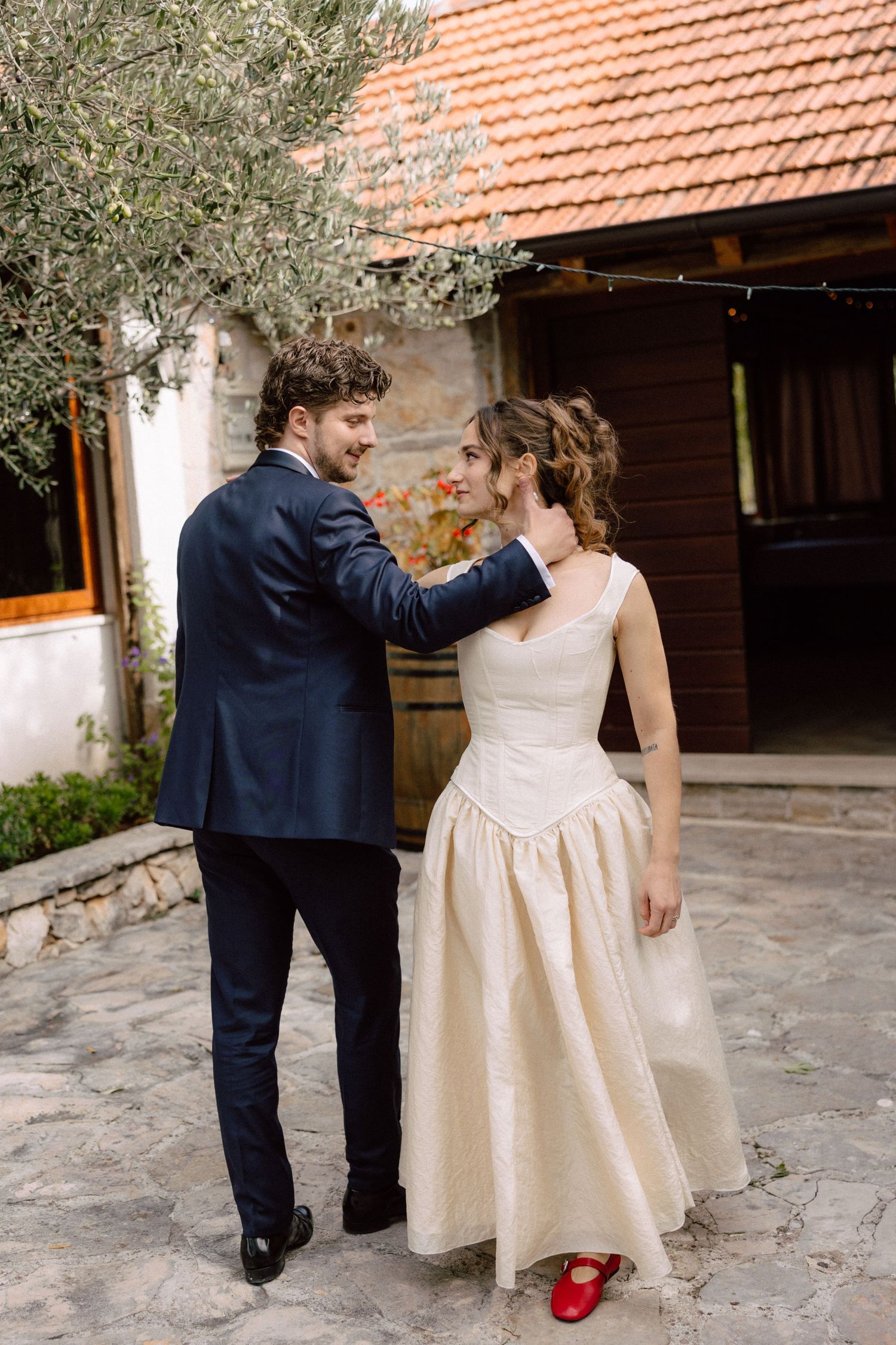 Wedding couple dancing outdoors on stone patio with terracotta roof in background.
