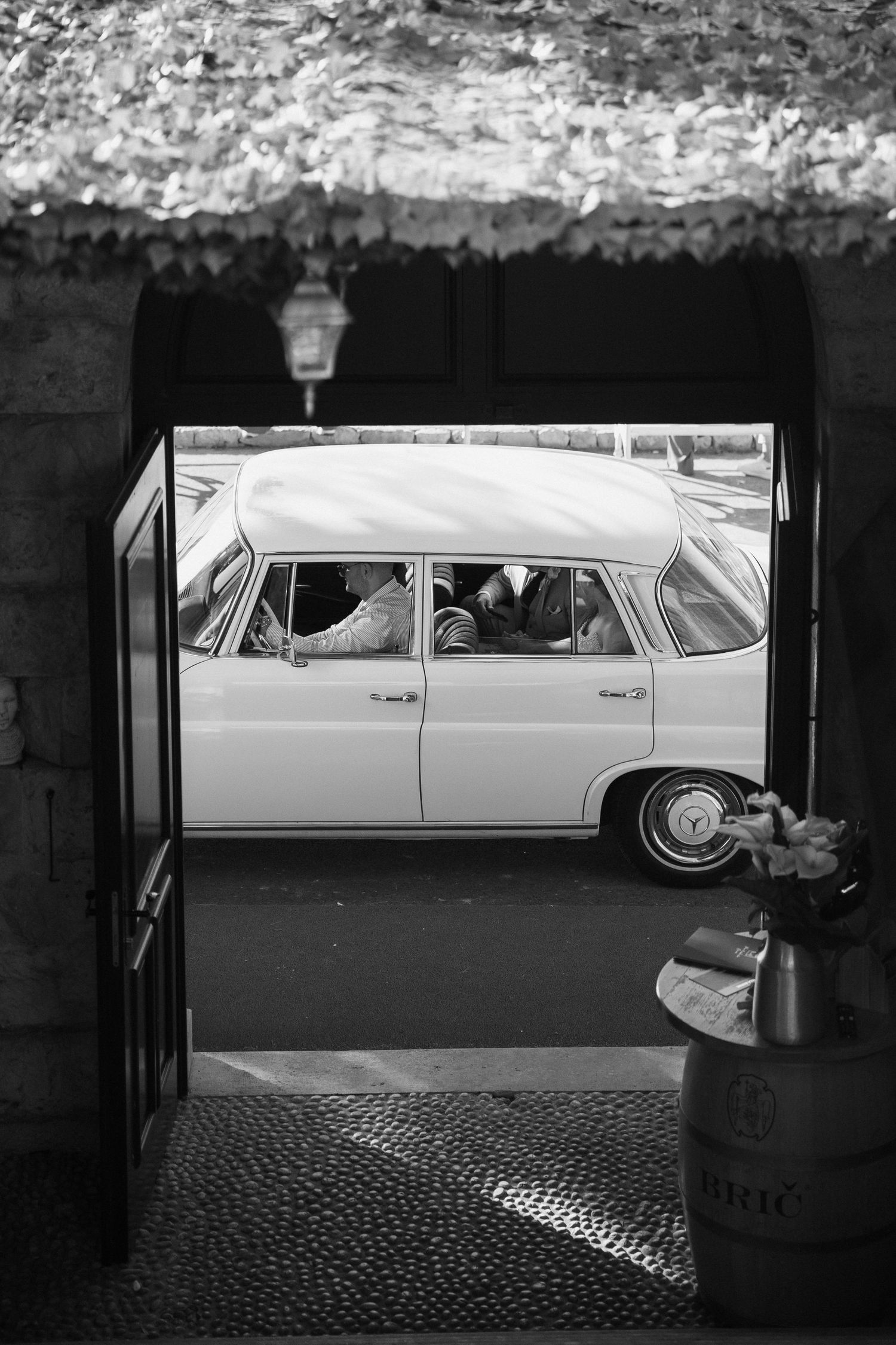 Vintage car viewed through stone archway entrance in black and white photography.