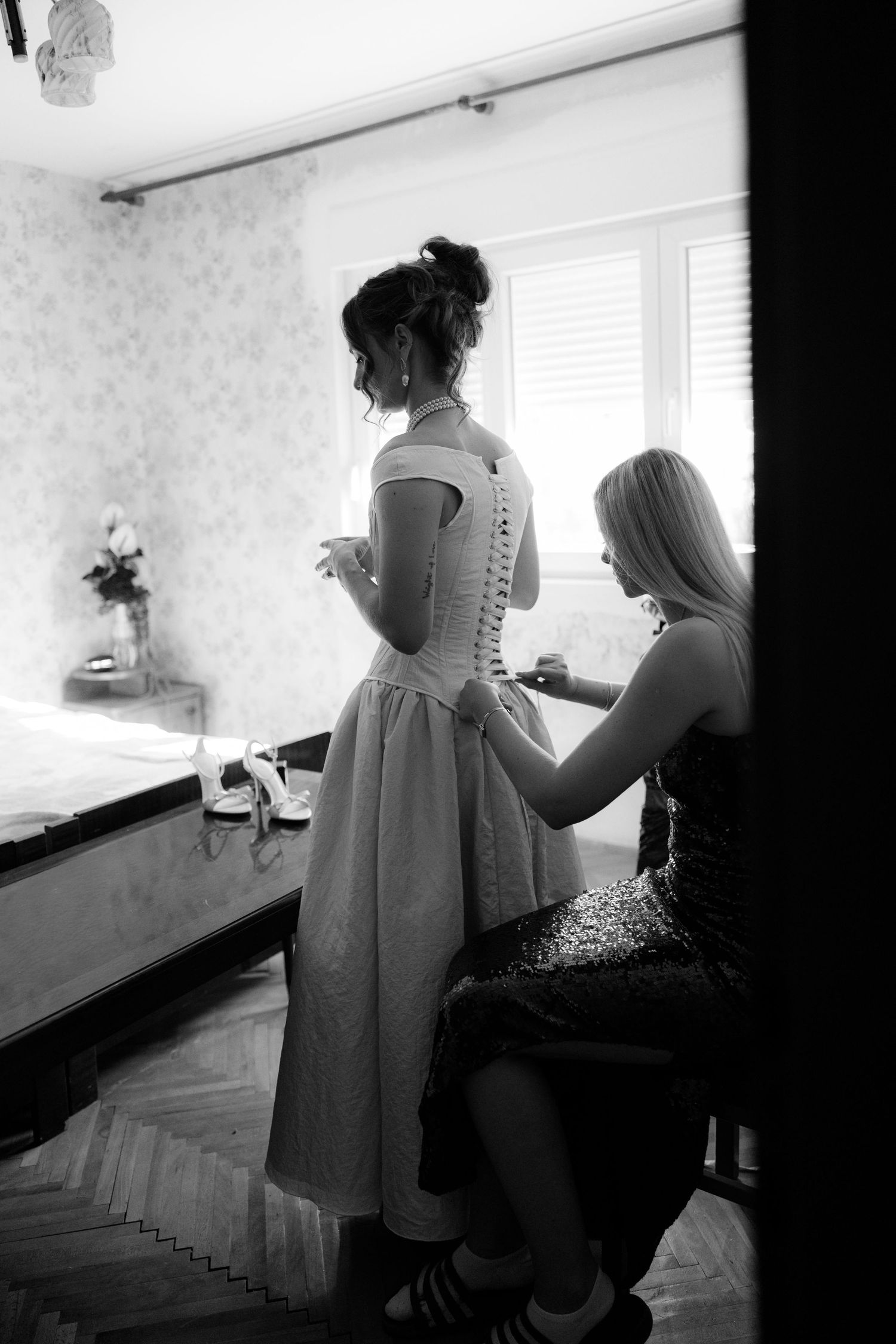 Black and white photo showing preparation moments with a white dress in an interior setting.