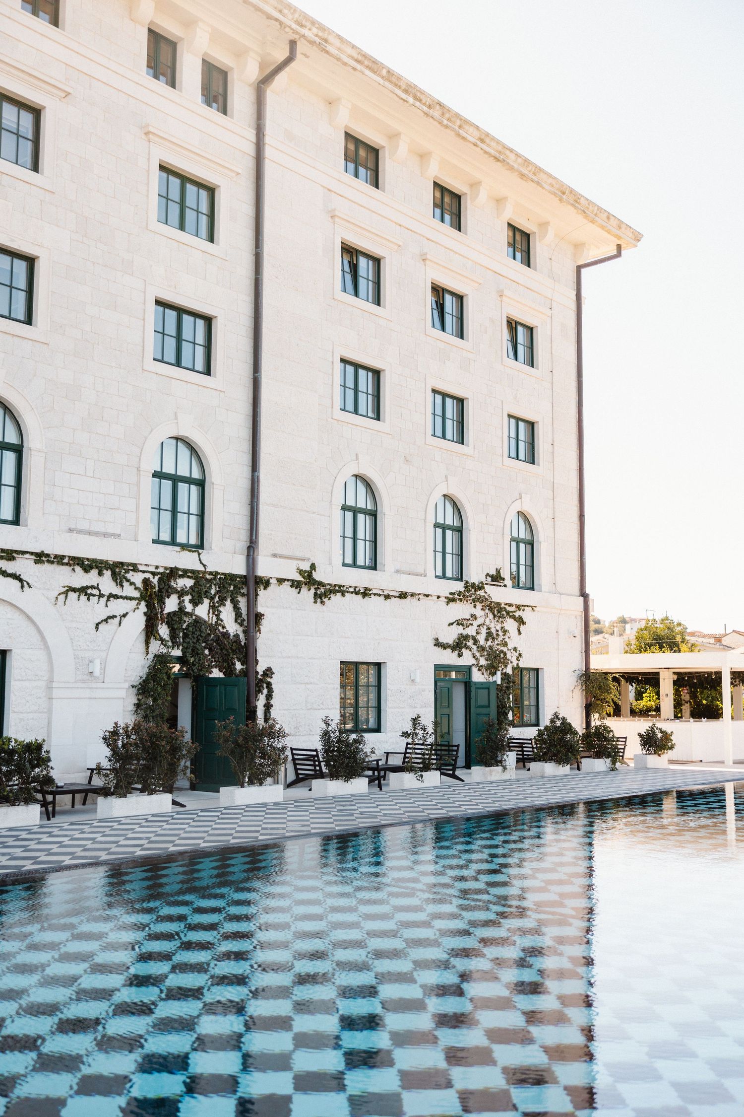 Elegant white hotel building with arched windows reflected in a checkered tile swimming pool.