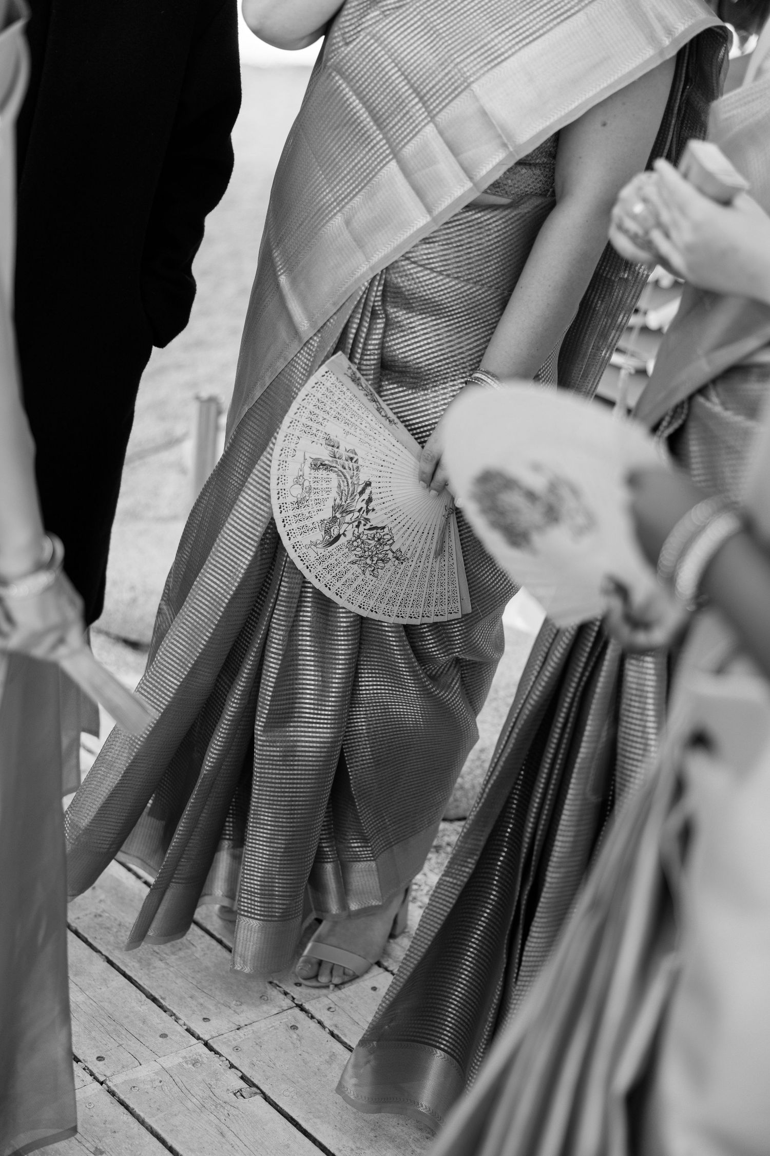 Black and white photo of women in traditional Indian sarees holding decorative fans at a cultural ceremony.