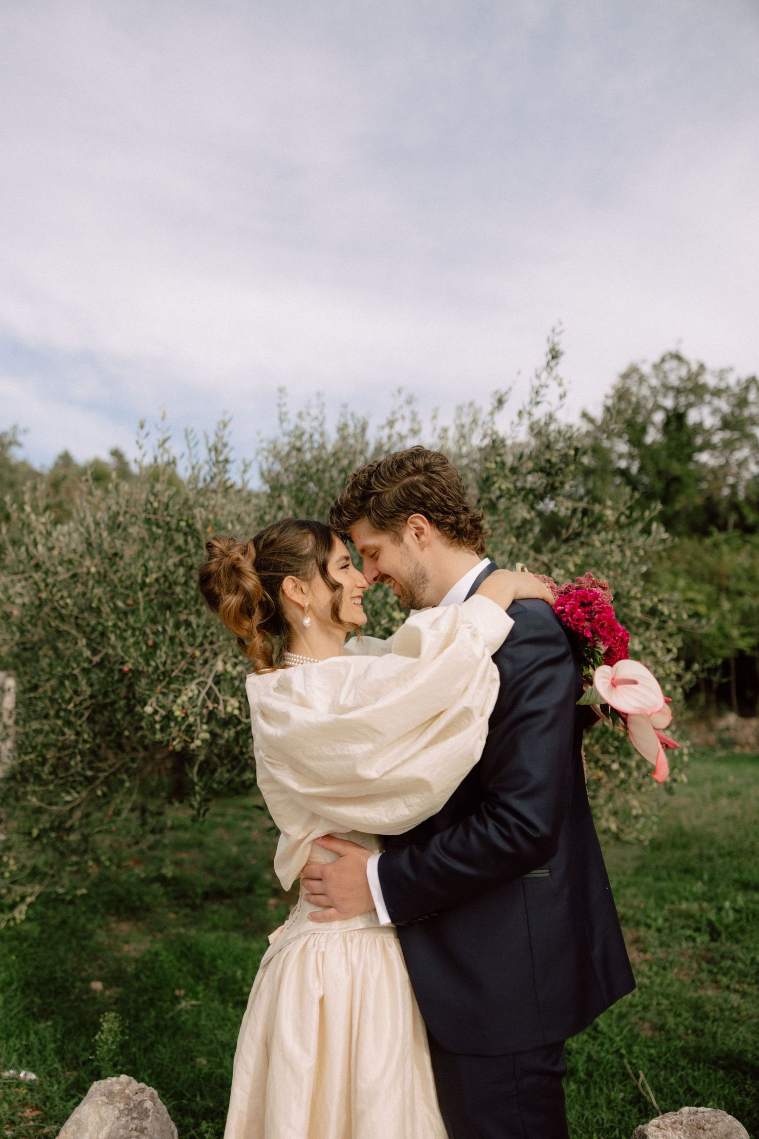 A romantic embrace between newlyweds in a garden setting with red flowers and natural greenery.