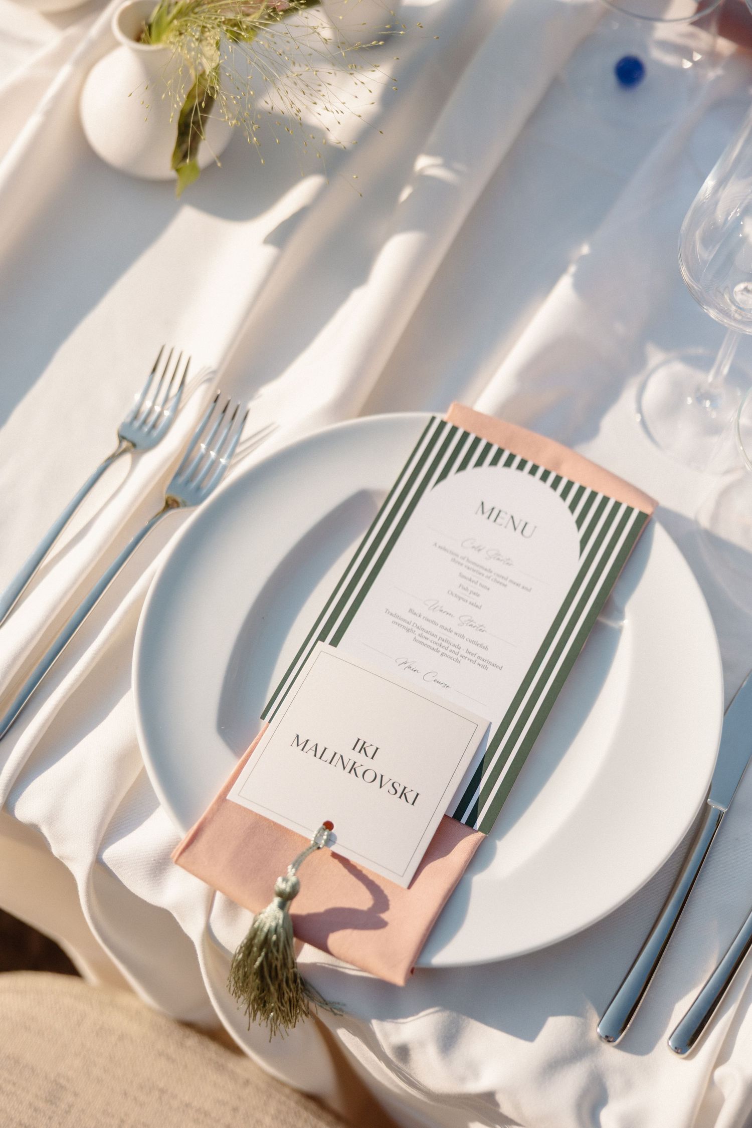 Elegant wedding place setting with striped menu card for IKI MALINKOVSKI on white tablecloth.