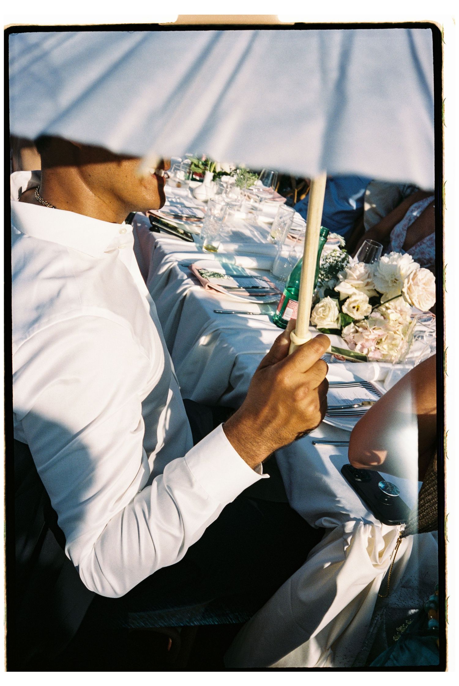 Groomsman holds candle at elegantly set outdoor wedding reception table.