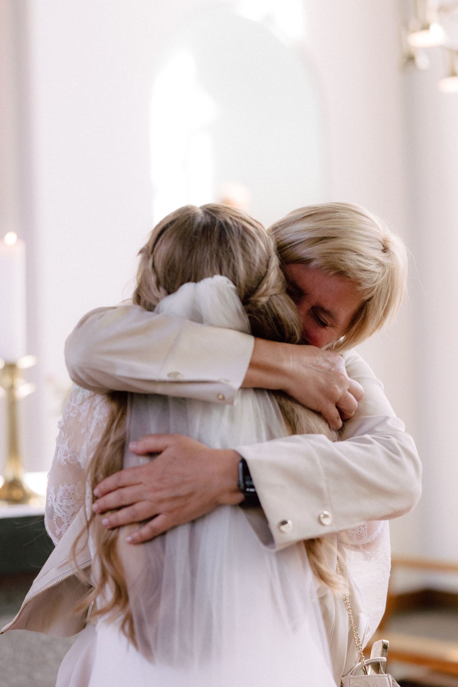 Emotional embraces shared during a wedding celebration in a light-filled space.