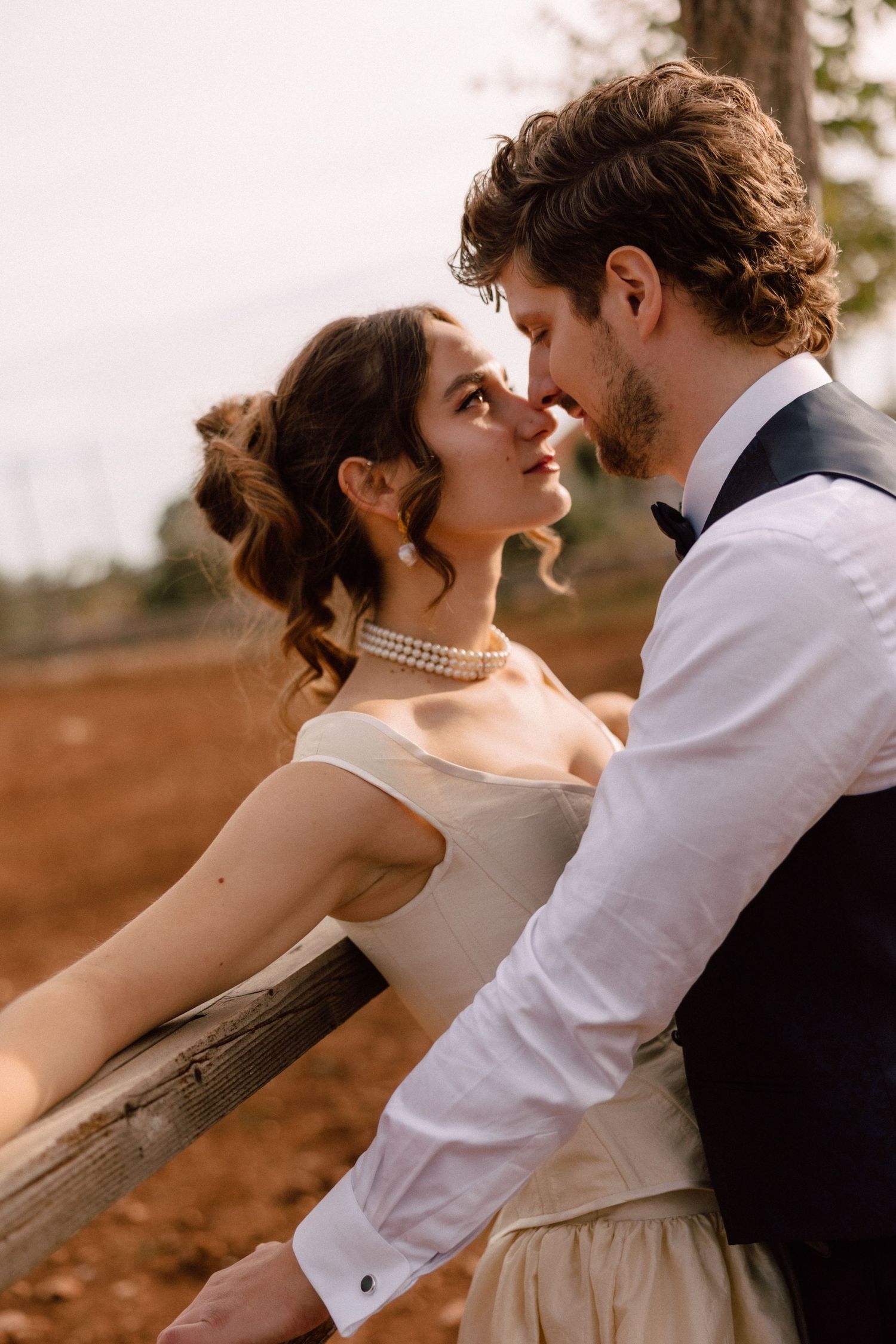 Romantic sunset moment between couple in wedding attire leaning against fence.